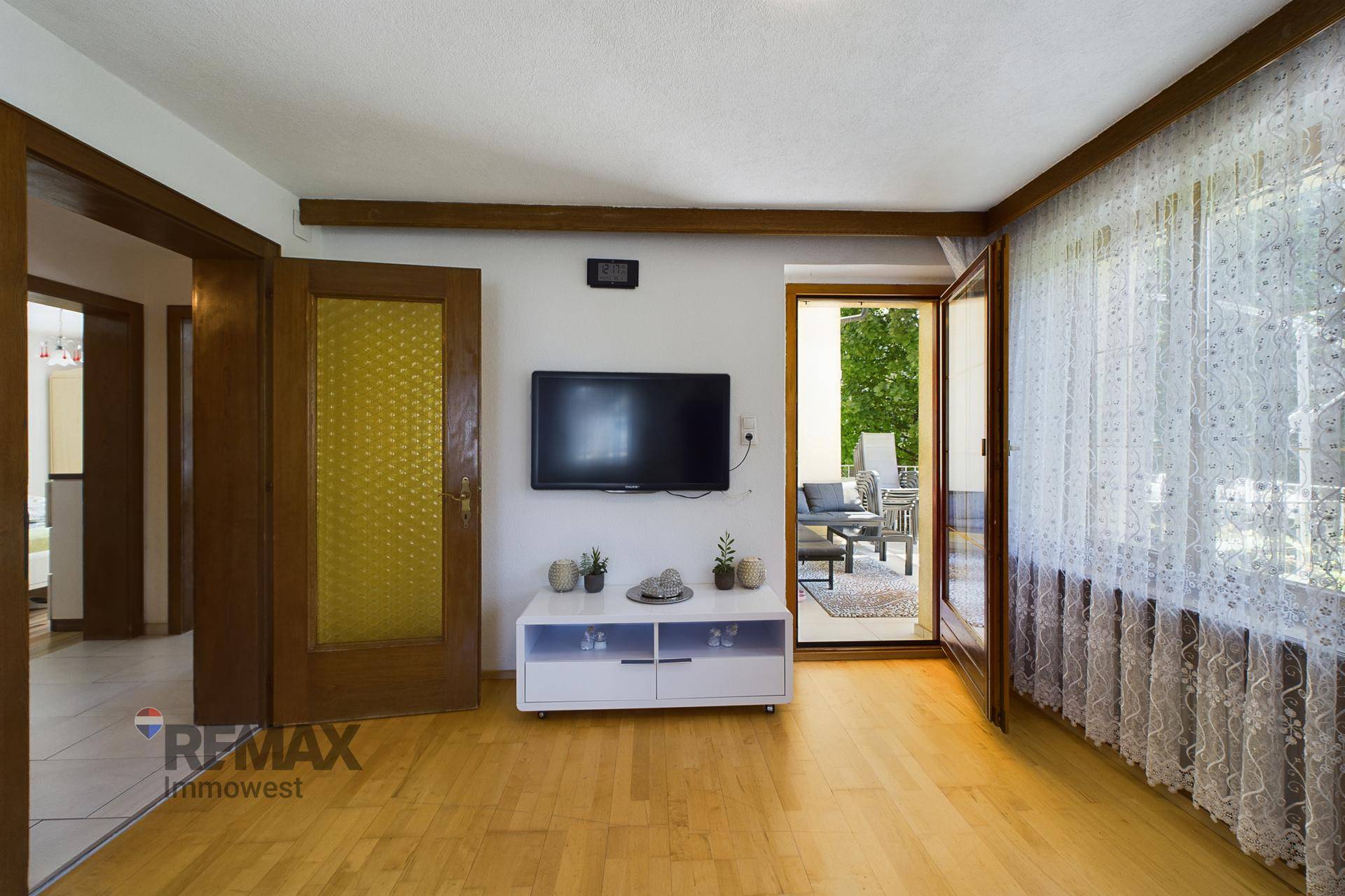 Wohnbereich mit Fernseher, Holzboden und Zugang zu einer möblierten Terrasse im Freien.