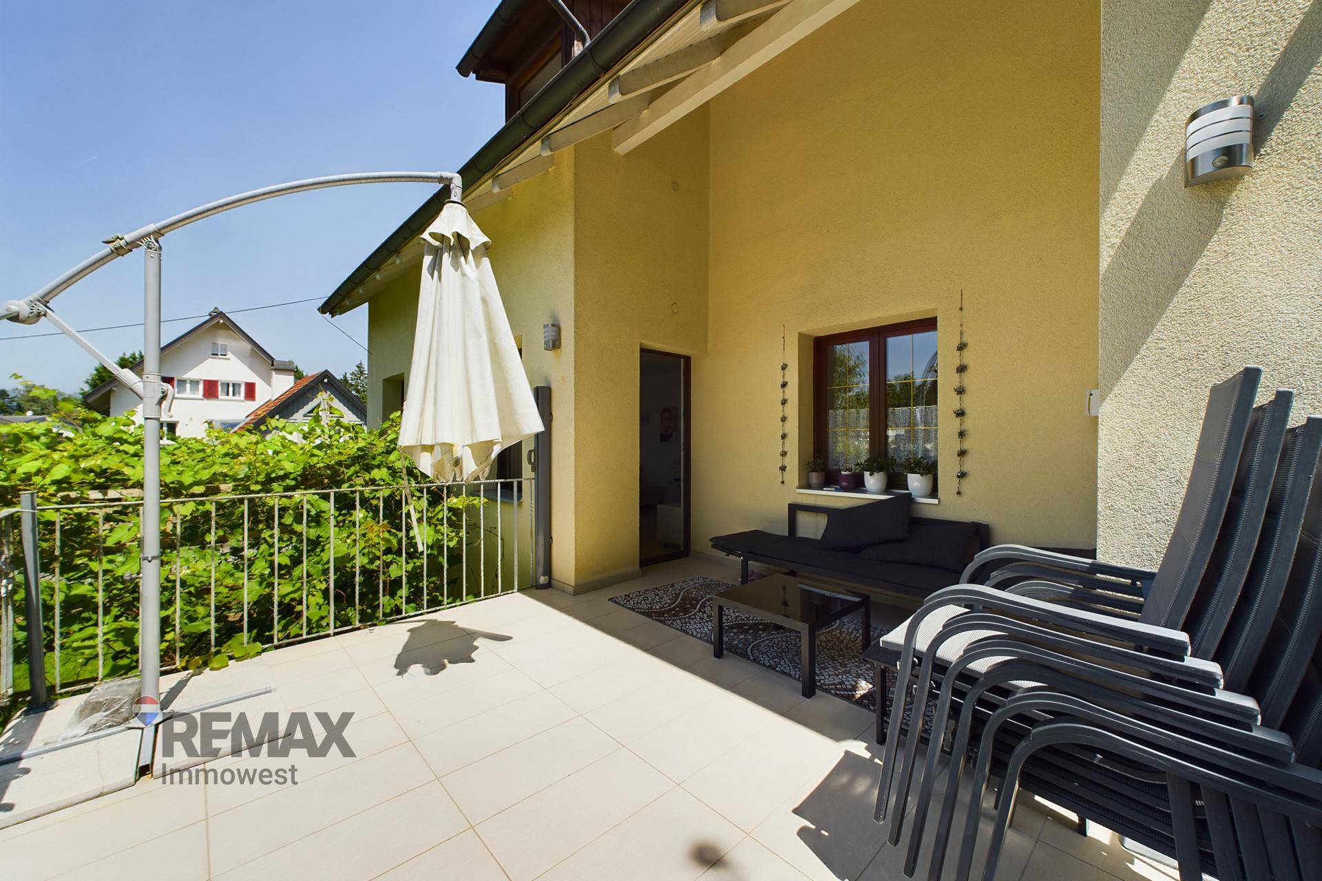 Geräumige Terrasse mit Sitzgelegenheiten und Sonnenschirm, direkt am Haus gelegen mit Blick auf die Umgebung.
