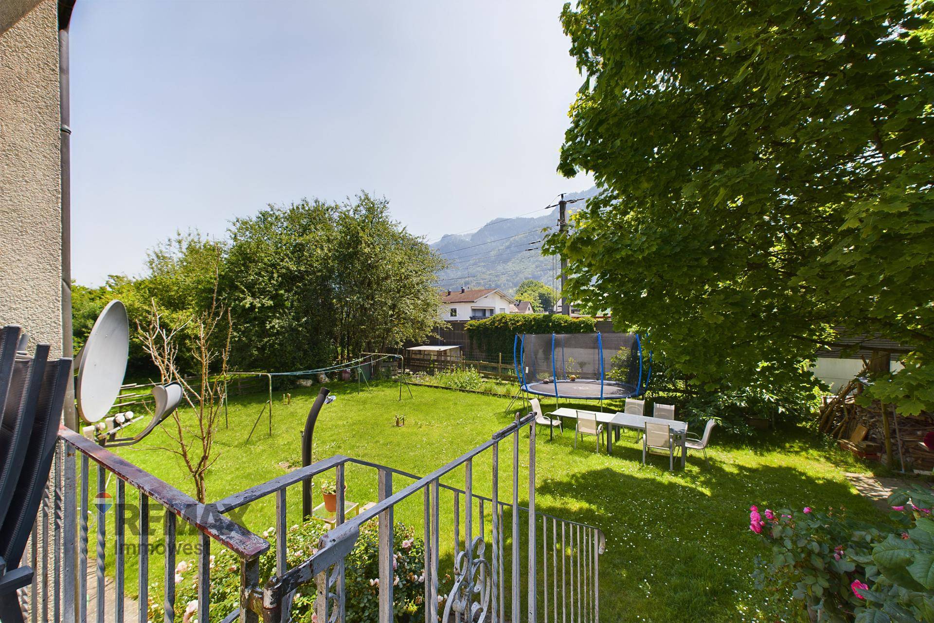 Großer Garten mit Rasenfläche, Trampolin und Esstisch im Freien, umgeben von Bäumen.