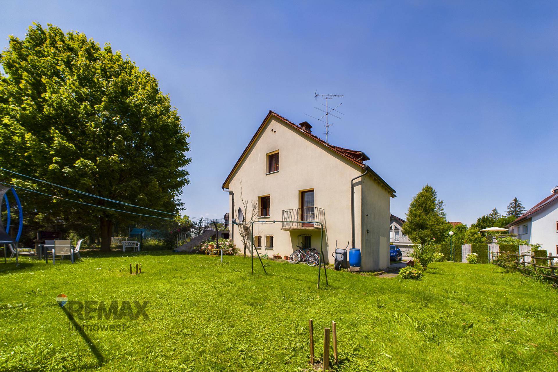 Rückansicht des Einfamilienhauses mit großem Garten, Rasenfläche und Balkon im Obergeschoss.