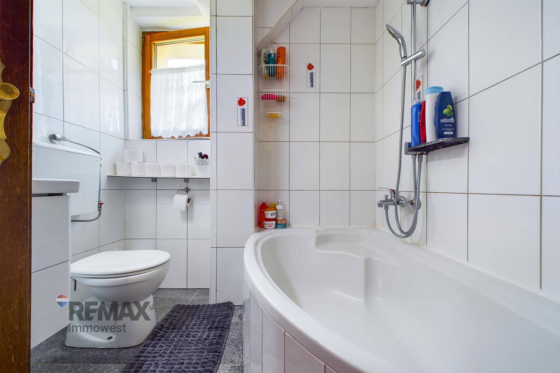 Gefliestes Badezimmer mit Badewanne, Toilette und Fenster, in einem funktionalen Design.
