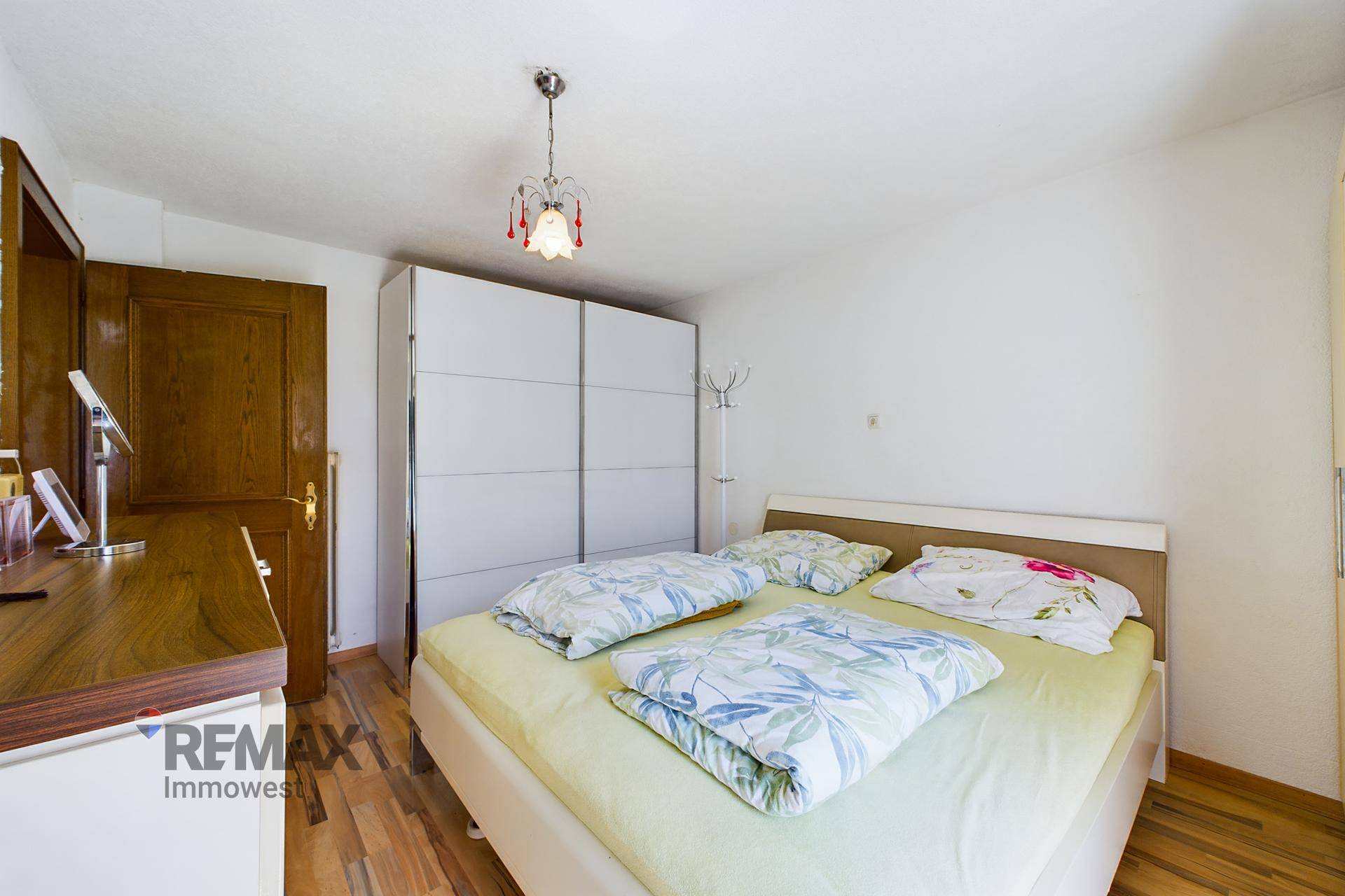 Helles Schlafzimmer mit Doppelbett, großem weißen Schiebetürenschrank und Holzboden.