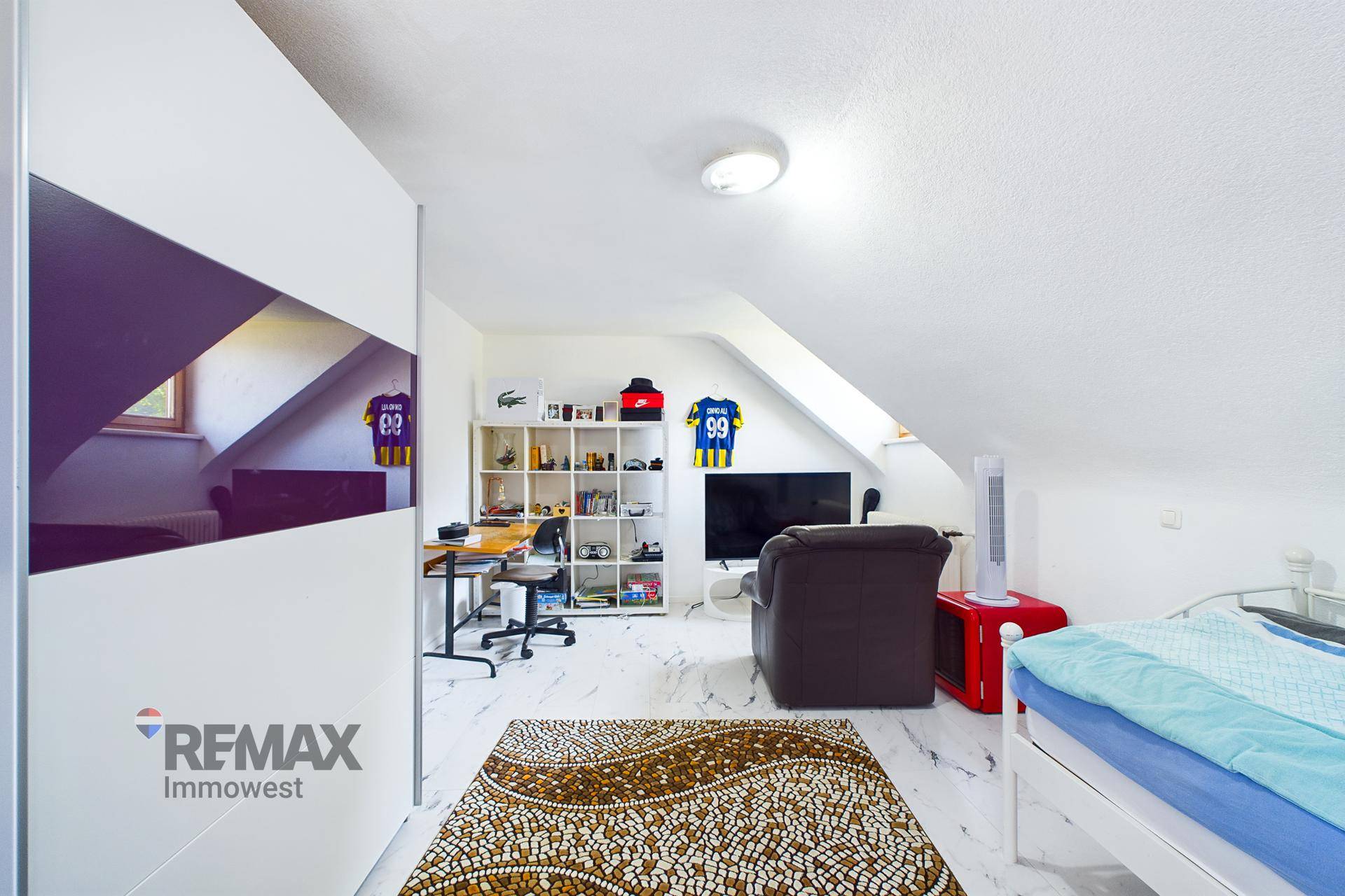 Geräumiges Dachzimmer mit Schrägen, als Schlaf- und Arbeitsbereich genutzt, mit modernem Teppich.