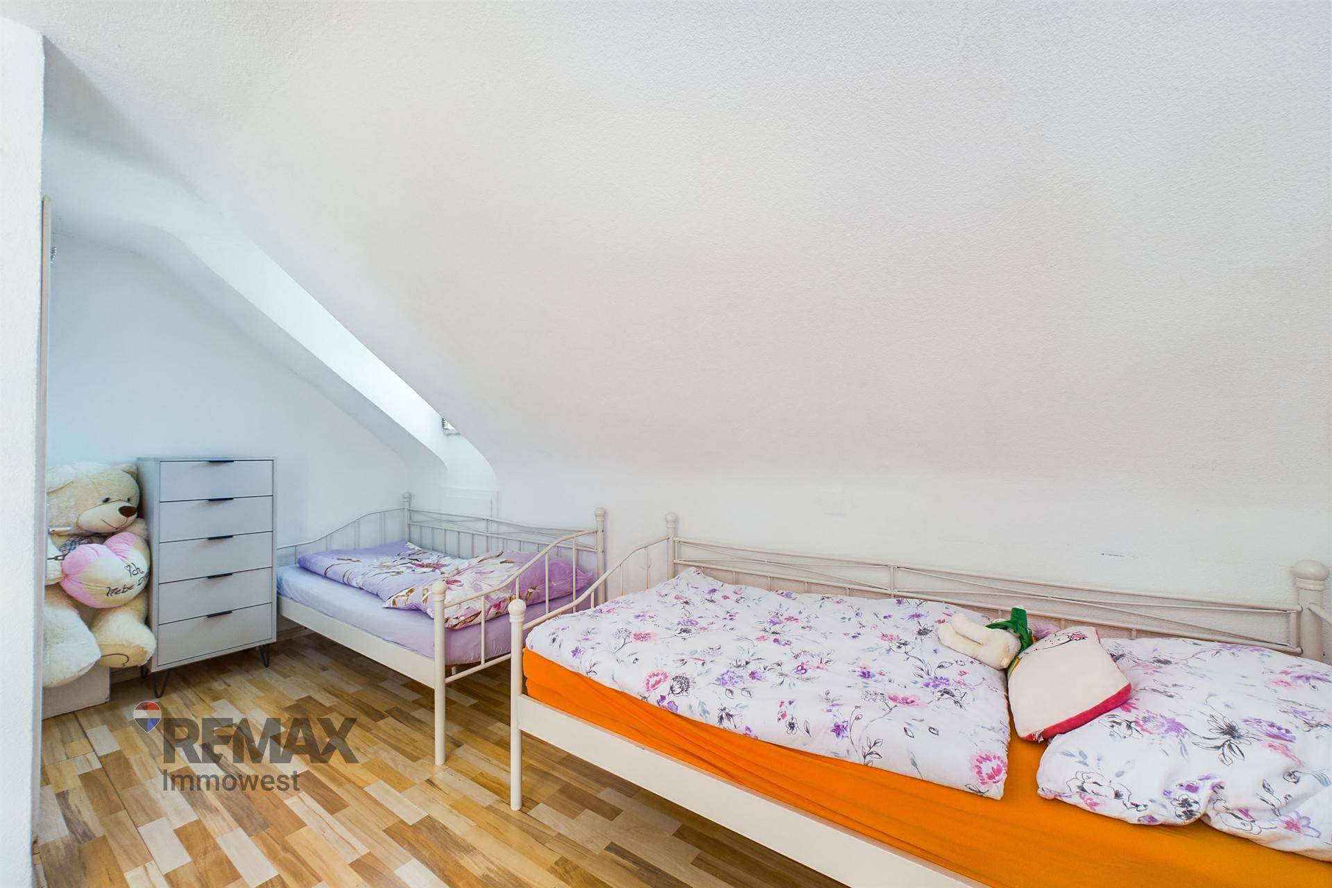 Helles Dachzimmer mit zwei Einzelbetten und Holzboden, ideal für Kinder oder Gäste.