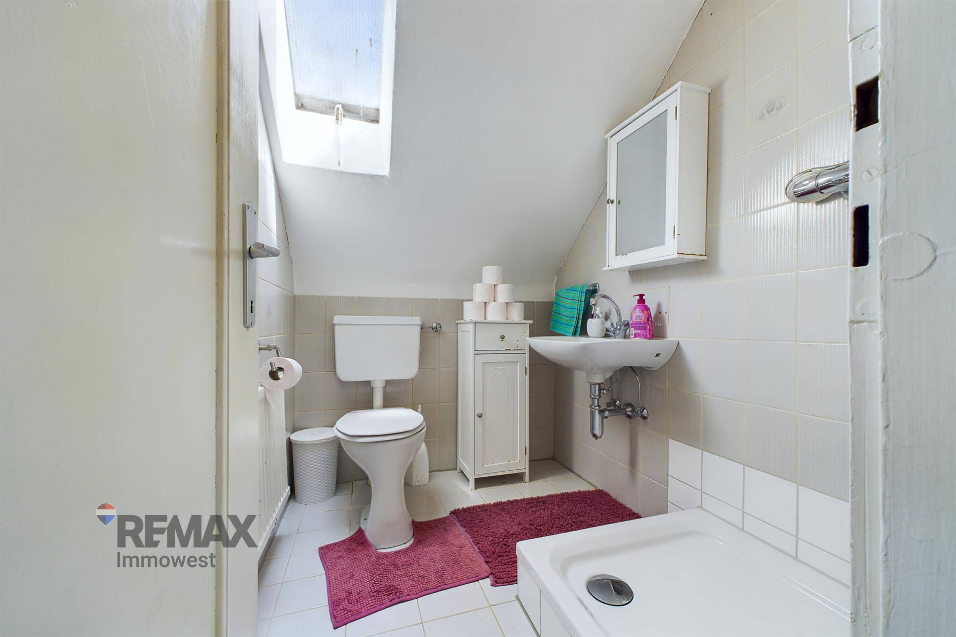 Dachbadezimmer mit Dusche, Toilette, Waschbecken und Dachfenster für natürliches Licht.
