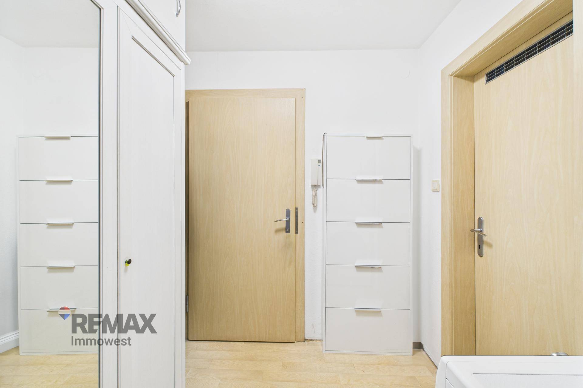 Heller Flur mit weißem Kleiderschrank, Kommode und Holztüren.