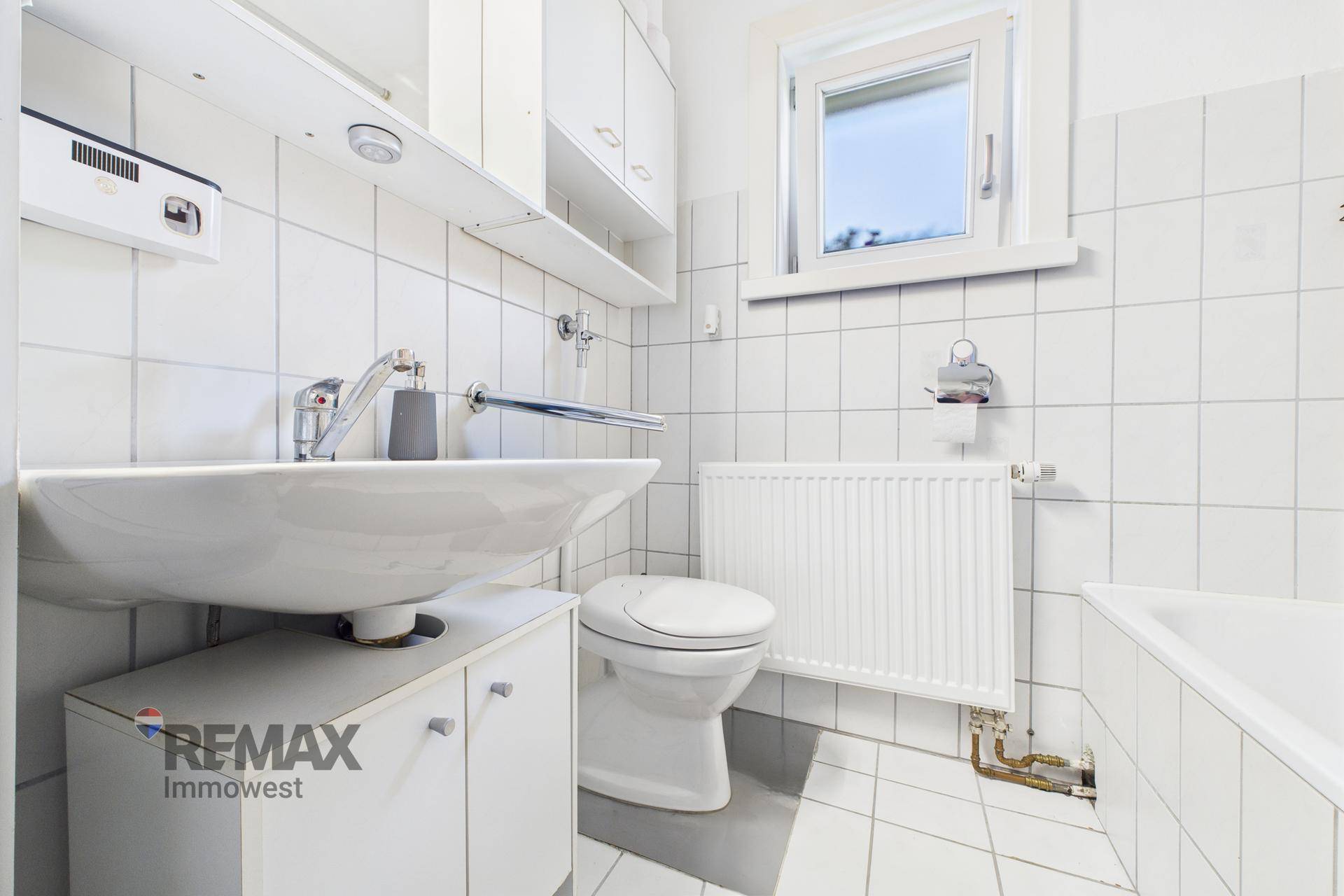 Gefliestes Badezimmer mit Waschbecken, Toilette, Badewanne und Fenster.