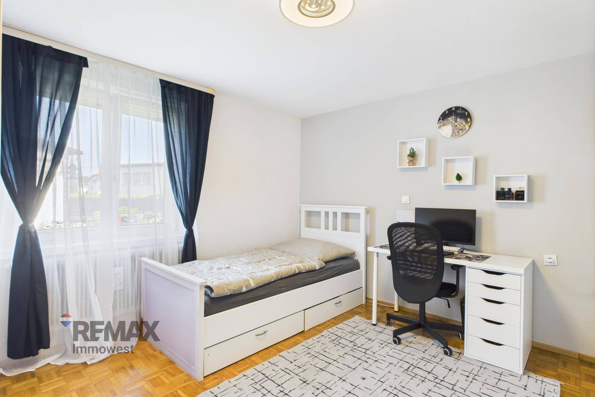 Helles Kinderzimmer mit Einzelbett, Schreibtisch und Fenster mit Vorhängen.