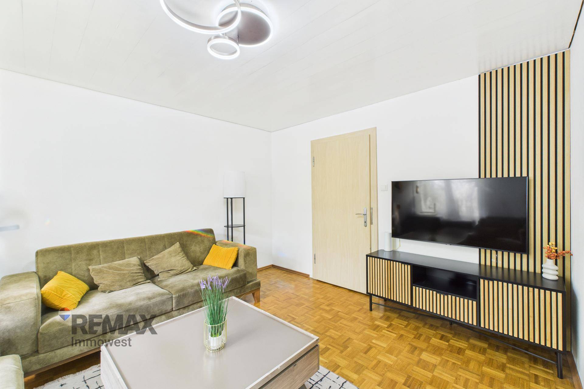 Gemütliches Wohnzimmer mit Sofa, Fernseher und modernem Wandpaneel.