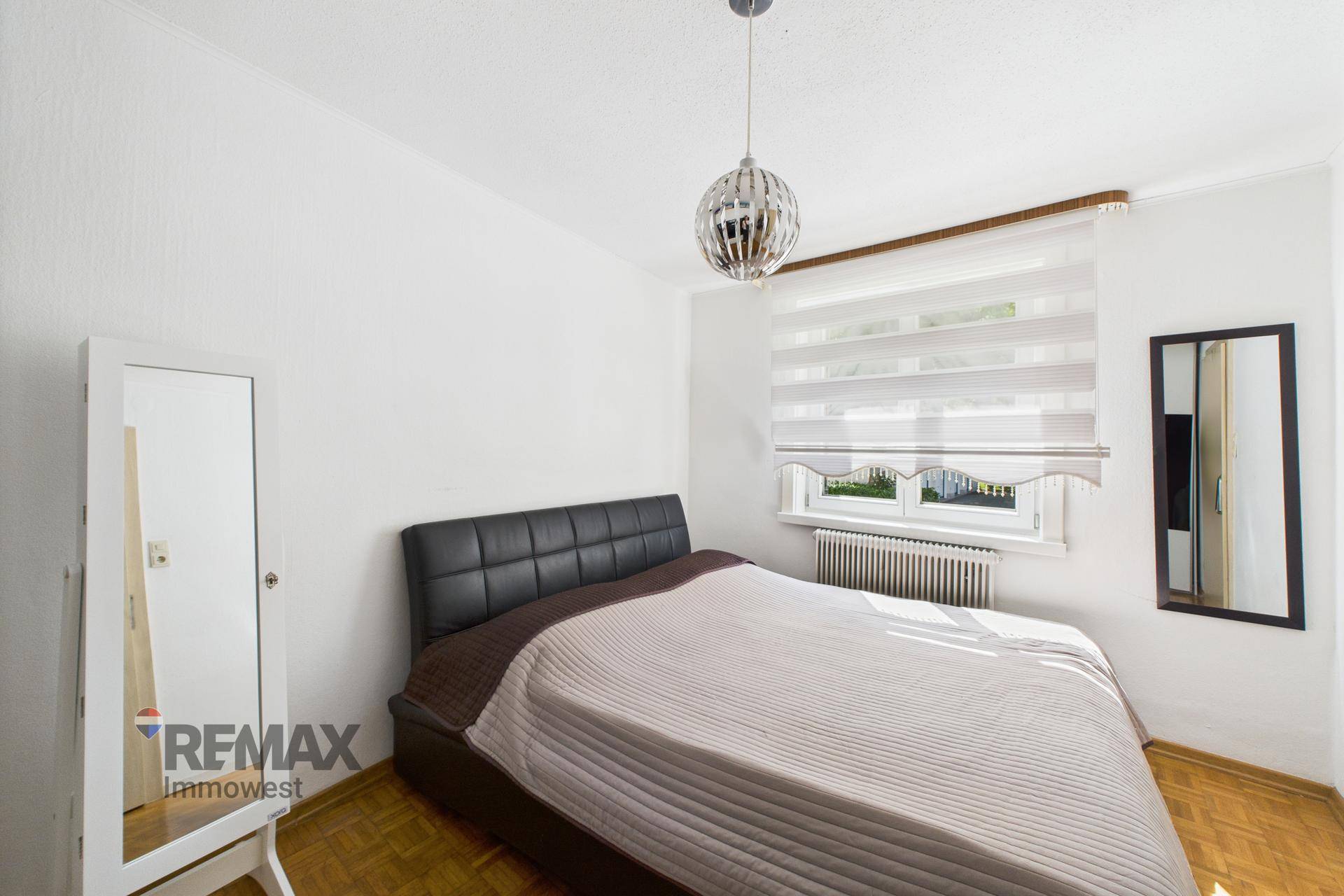 Helles Schlafzimmer mit Doppelbett, Fenster und Nachttisch.