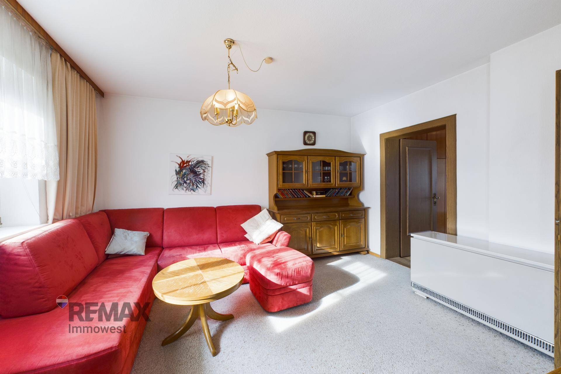 Gemütliches Wohnzimmer mit rotem Sofa, Teppichboden und traditionellen Holzmöbeln.