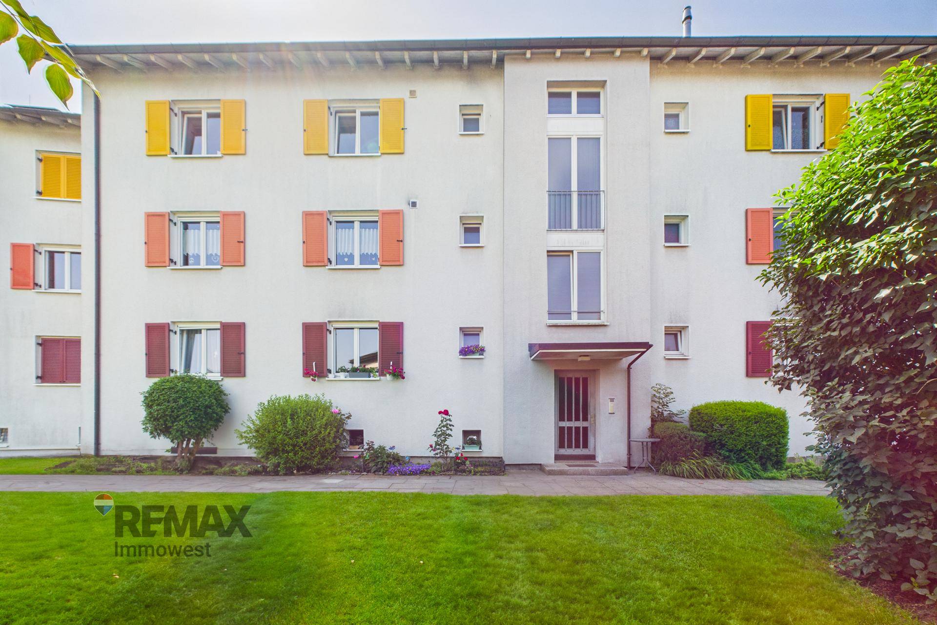 Mehrfamilienhaus mit farbigen Fensterläden und gepflegter Grünfläche.