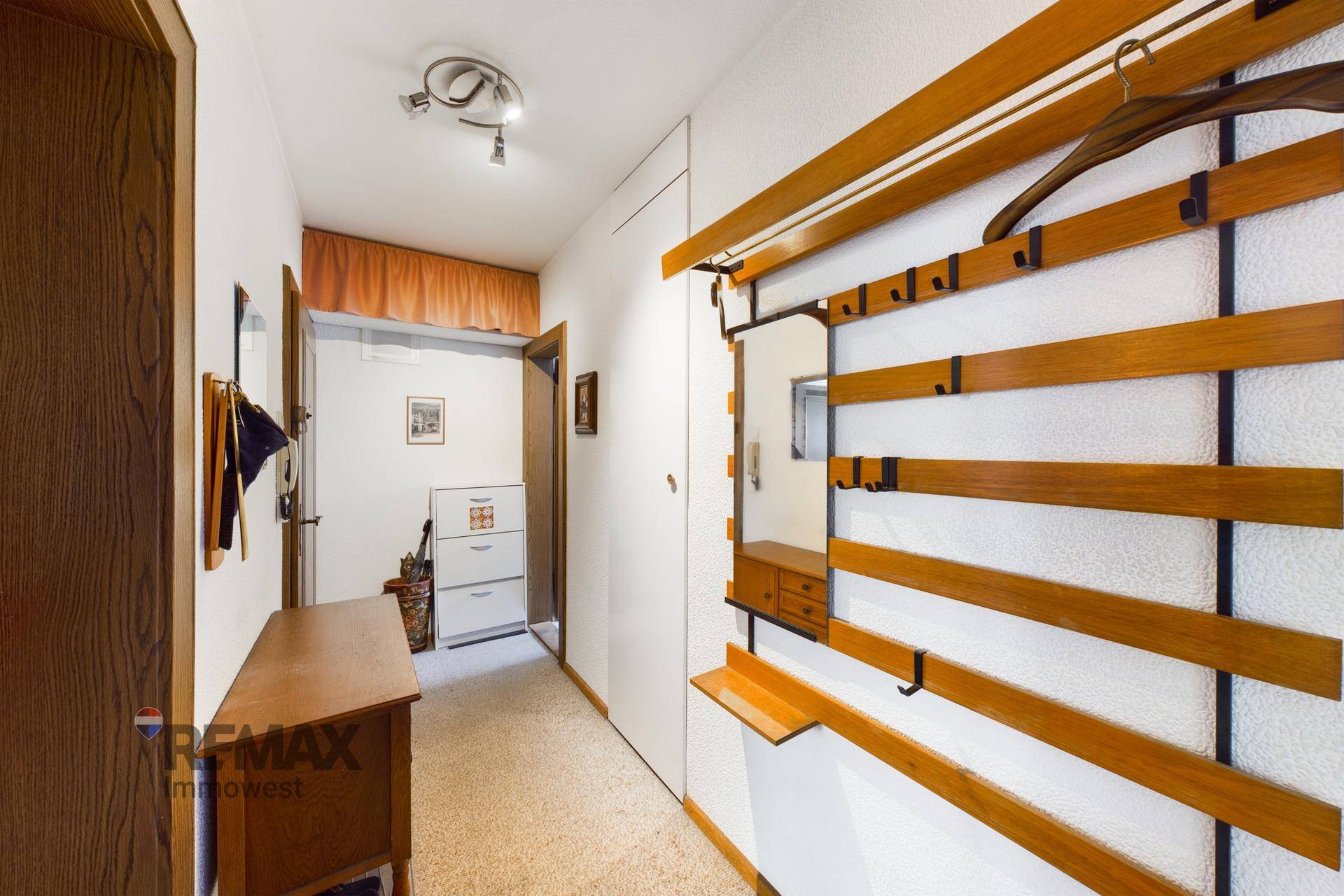 Heller Flur mit Garderobe, Spiegel und Teppichboden, der zu weiteren Räumen führt.
