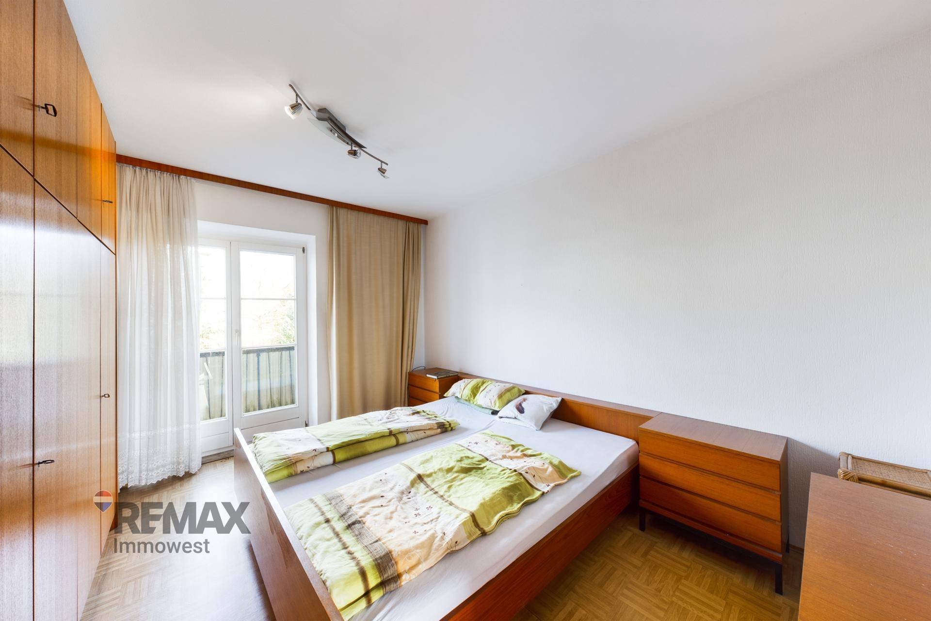 Schlafzimmer mit Doppelbett, Holzschränken und Zugang zu einem Balkon.