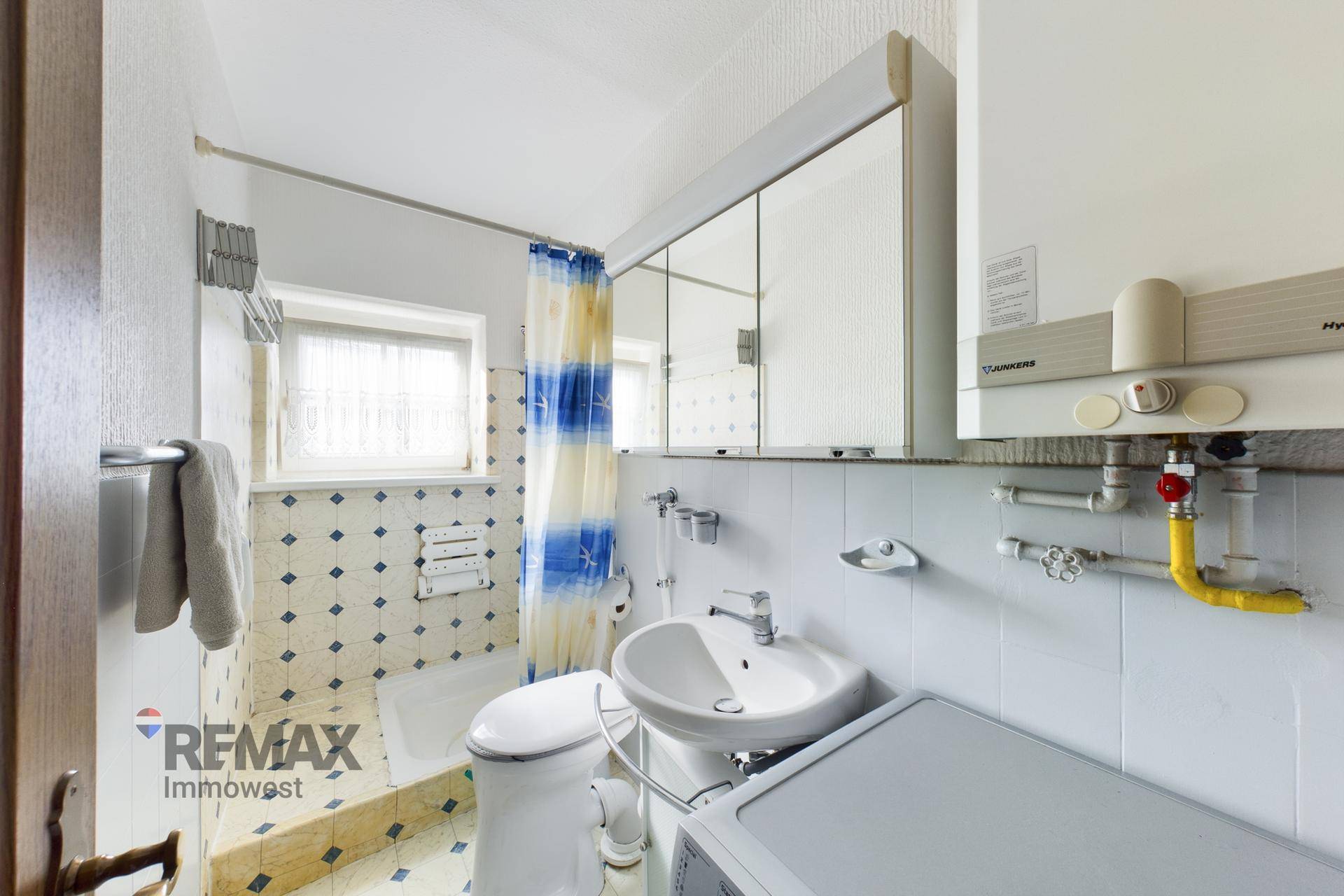Badezimmer mit Badewanne, Waschbecken und WC, ausgestattet mit blauen Fliesen und Boiler.