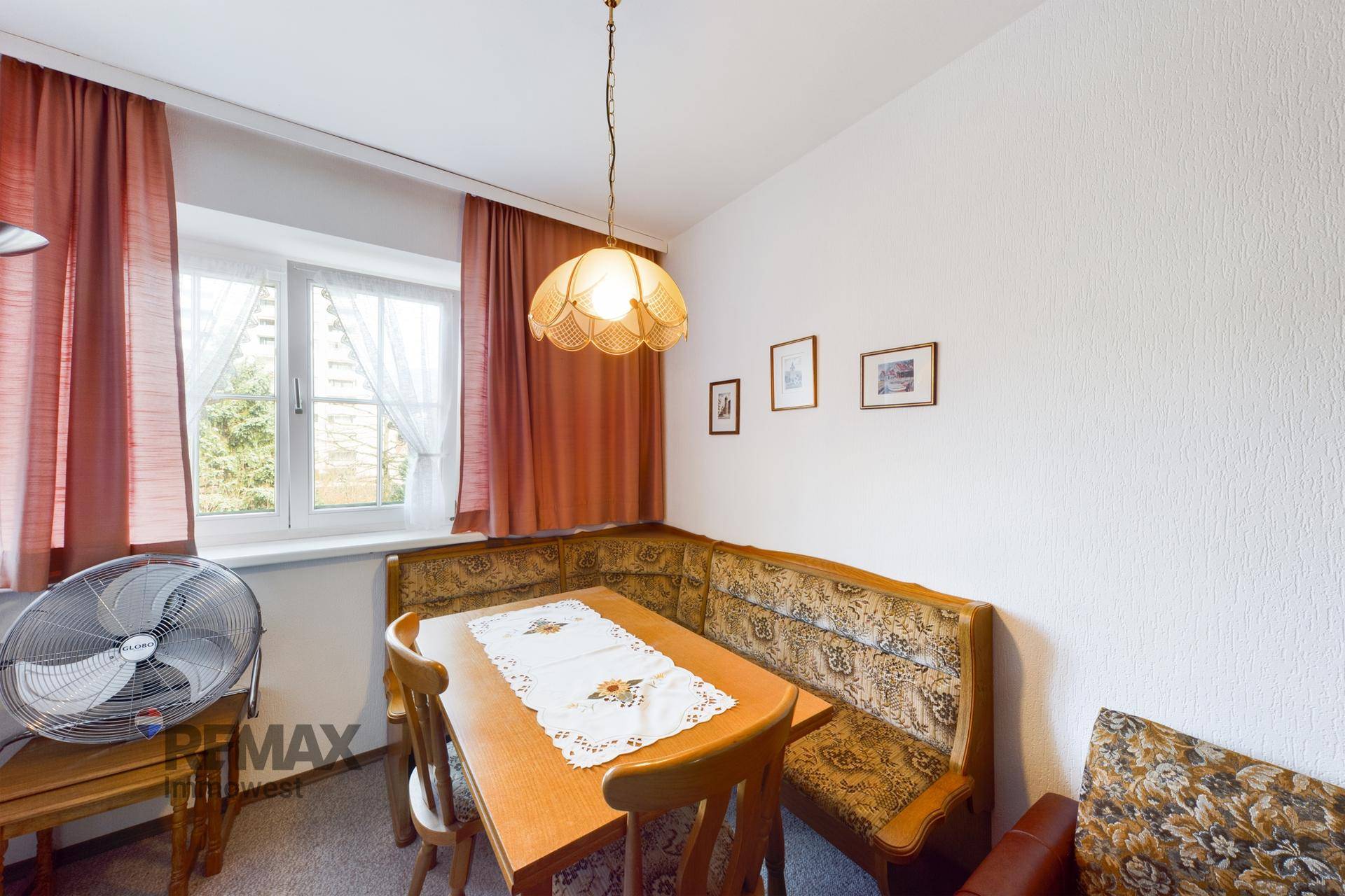 Detailansicht des Essbereichs mit traditioneller Eckbank, Holztisch und Fenster mit Vorhängen.