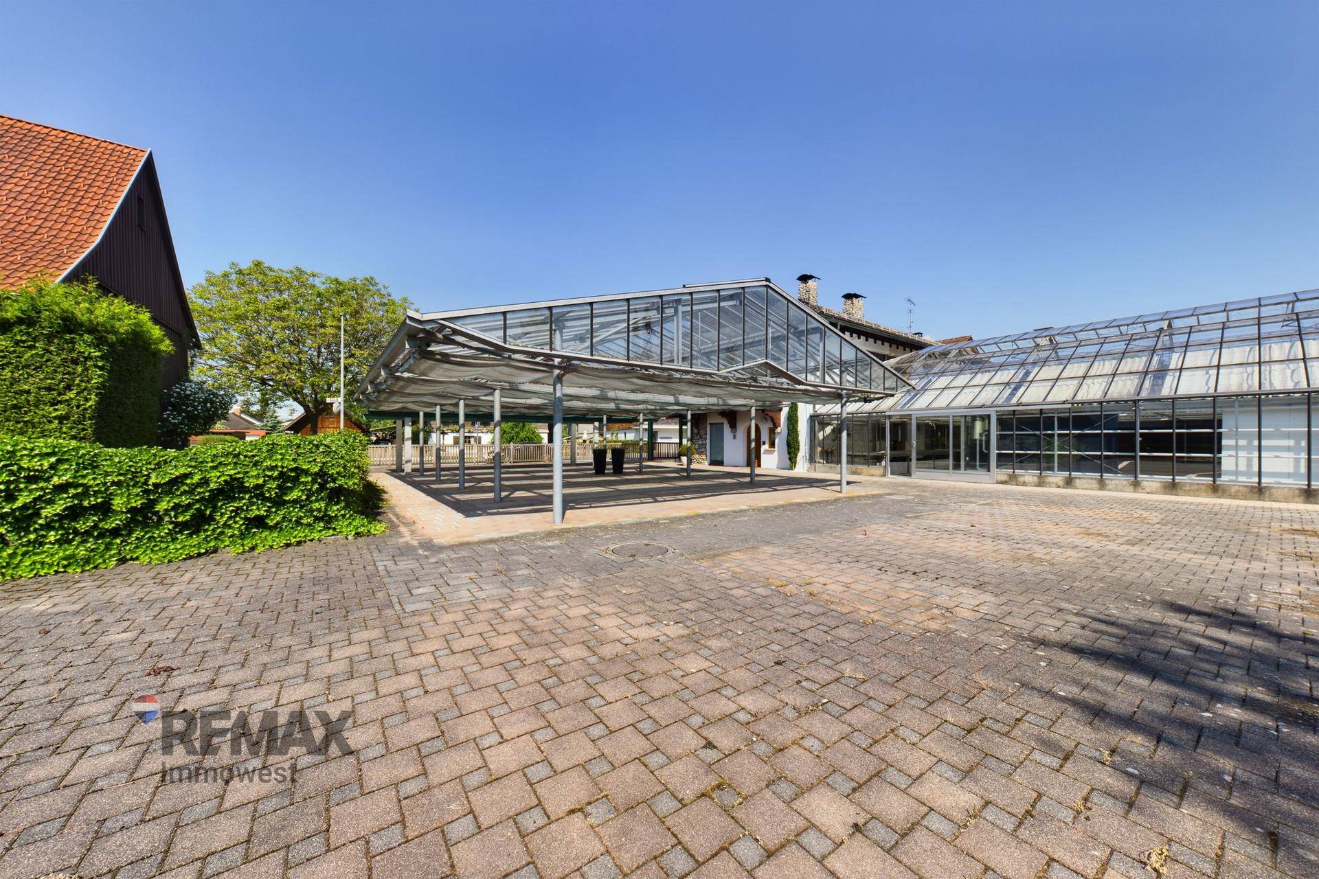 Weitläufiger gepflasterter Vorplatz mit überdachten Parkplätzen und dem Hauptgebäude im Hintergrund.