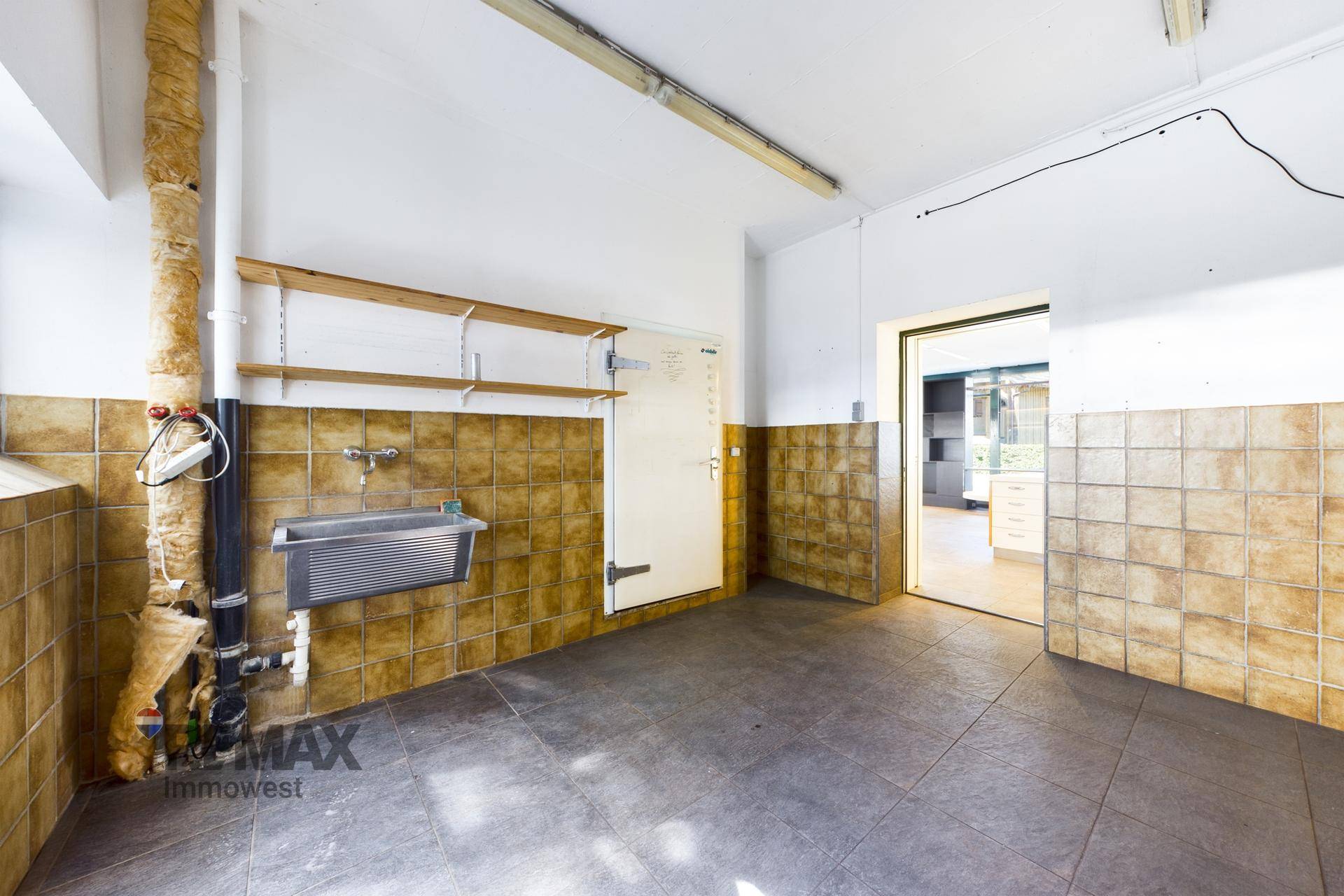 Hauswirtschaftsraum mit gefliesten Wänden, Waschbecken und Zugang zu anderen Räumen.