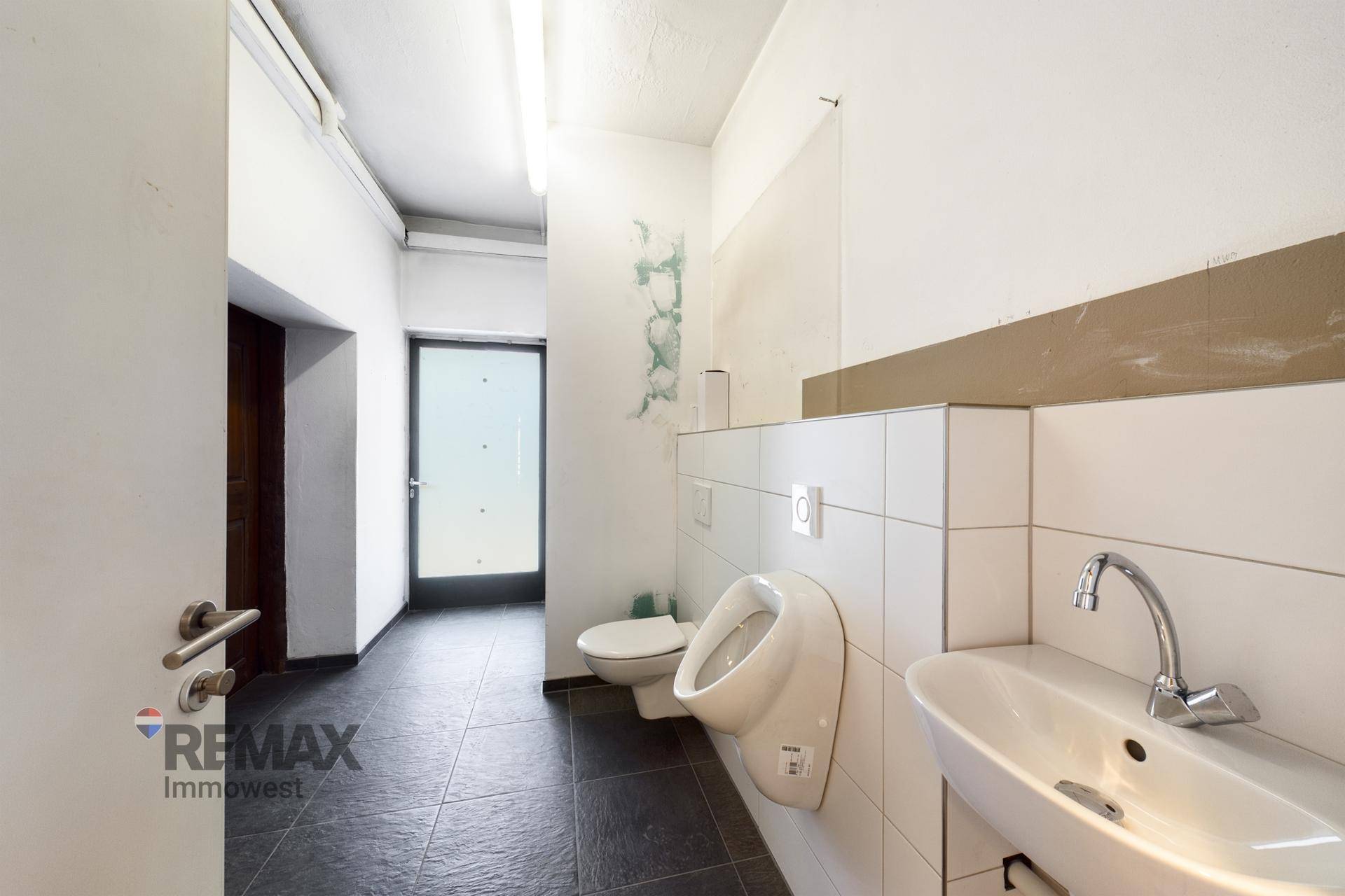 Gästetoilette mit Urinal, WC, Waschbecken und Fliesenboden.