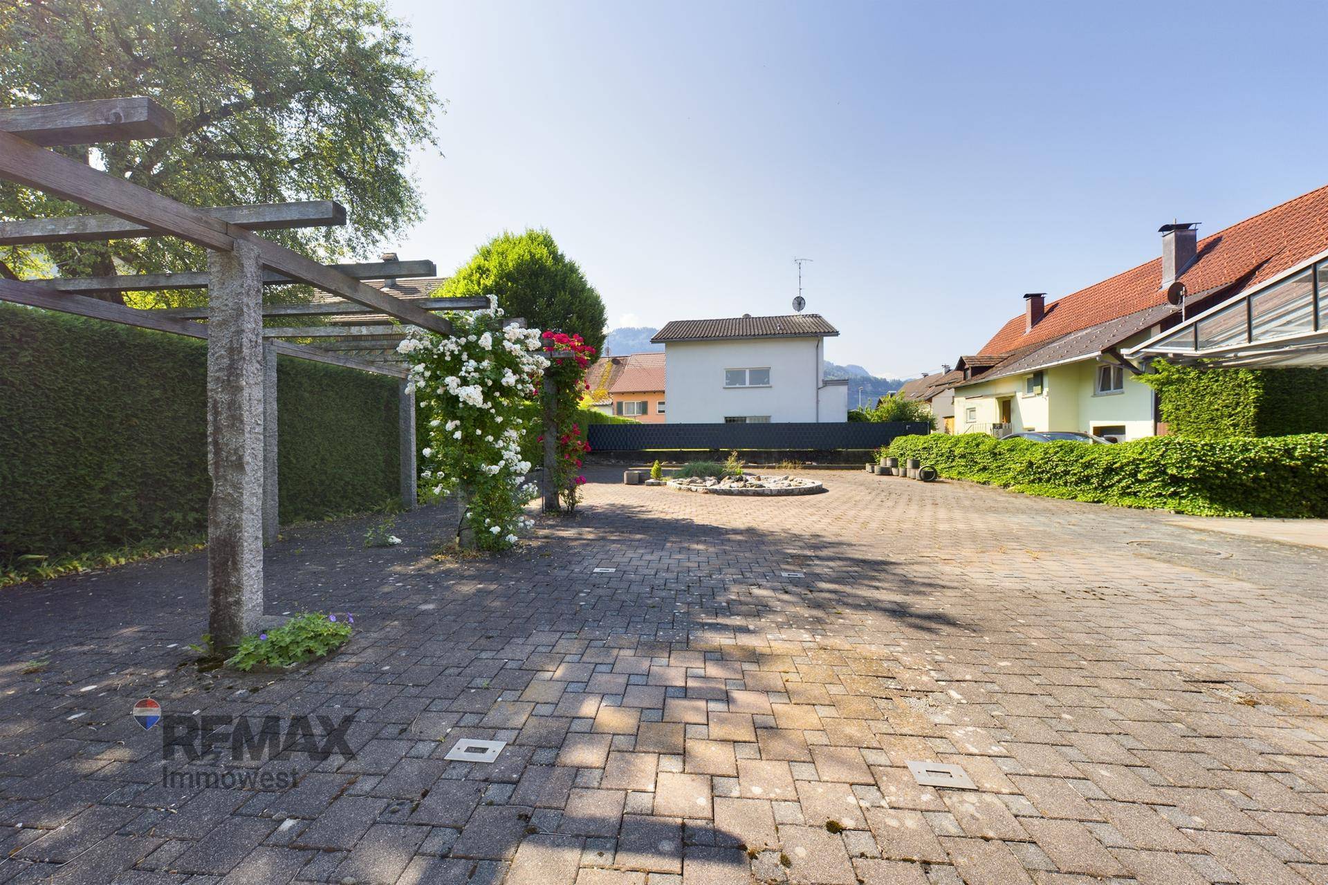 Gepflasterter Außenbereich mit Pergola, Rosen und Blick auf die umliegenden Gebäude.