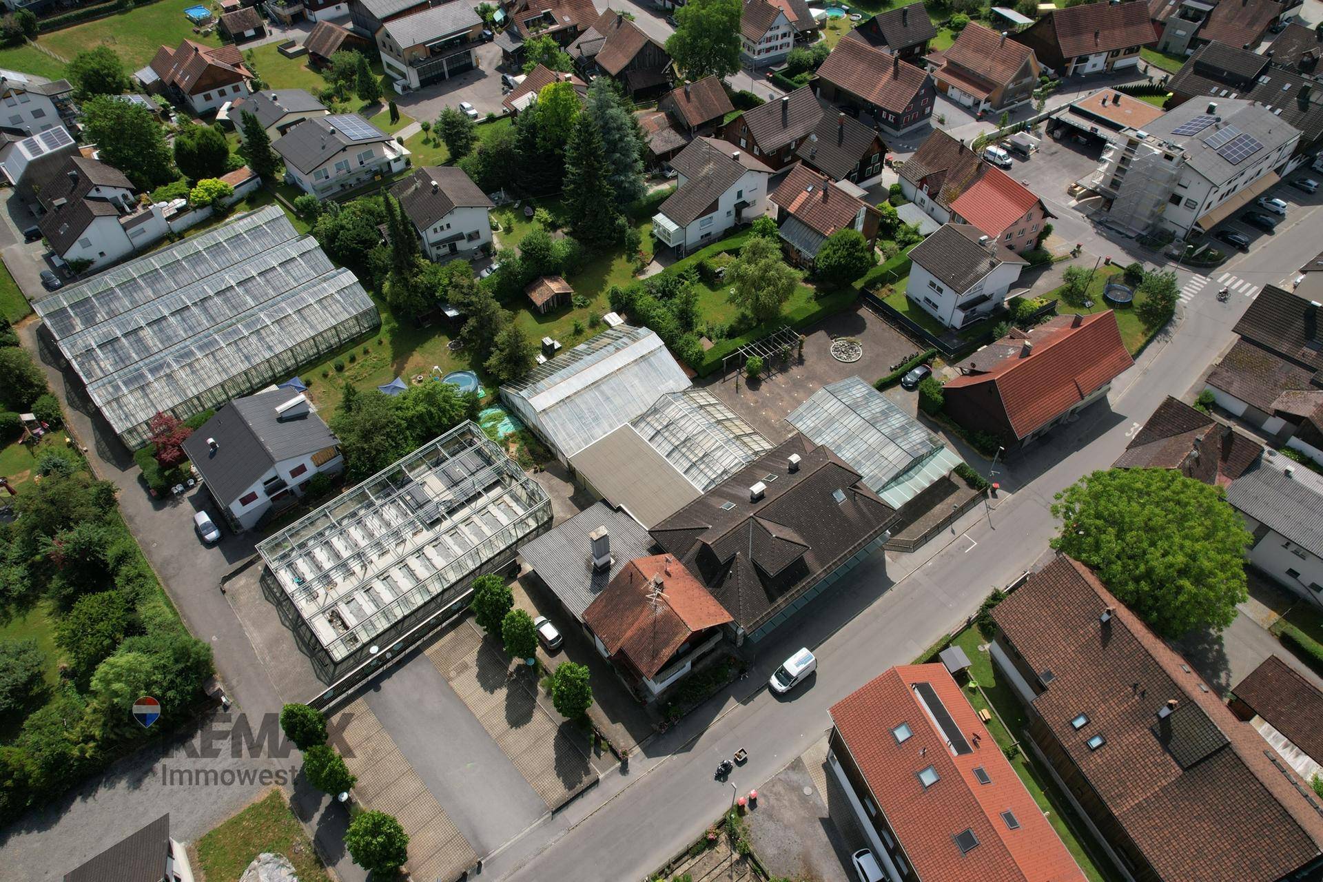 Luftaufnahme eines Gewerbegebiets mit Gewächshäusern, Gebäuden und umliegenden Wohngebieten.
