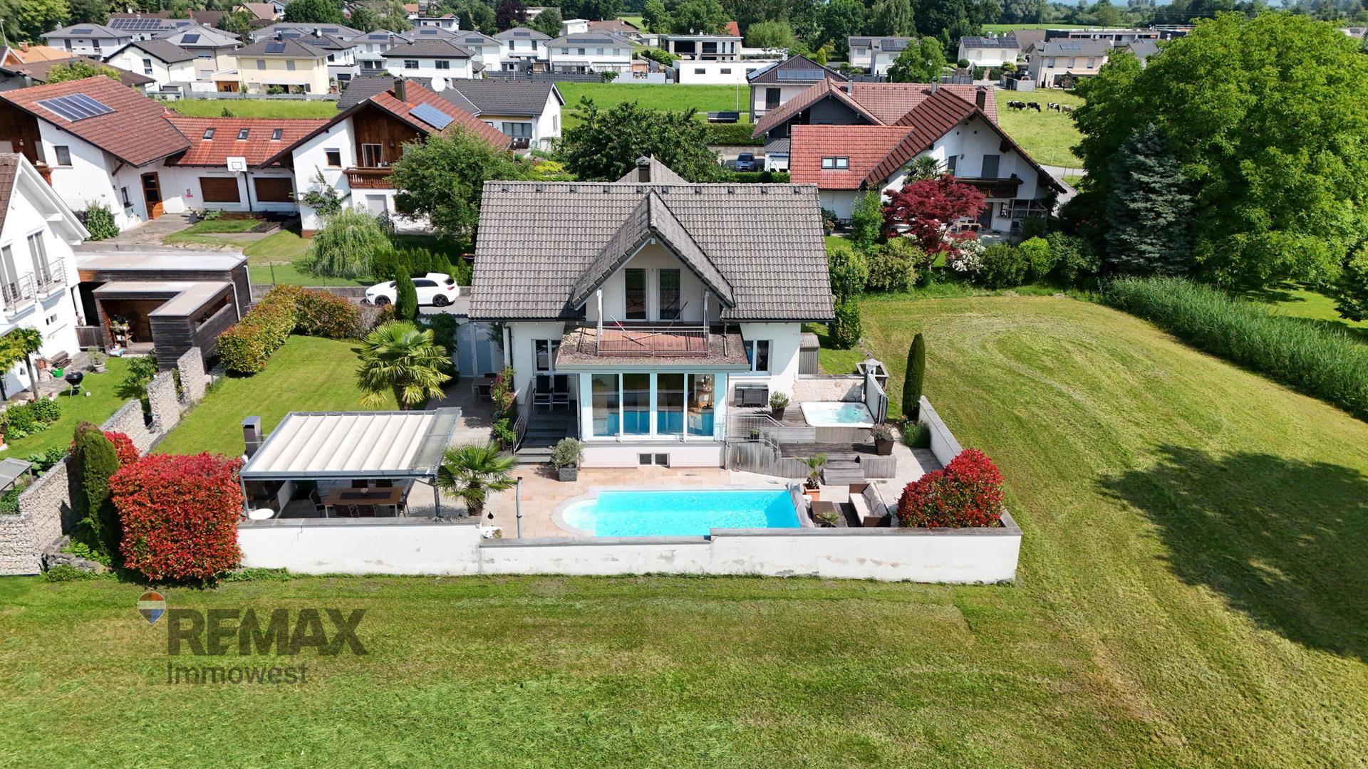 Luftaufnahme des Hauses mit Pool, Garten und umliegender Wohnsiedlung in grüner Umgebung.
