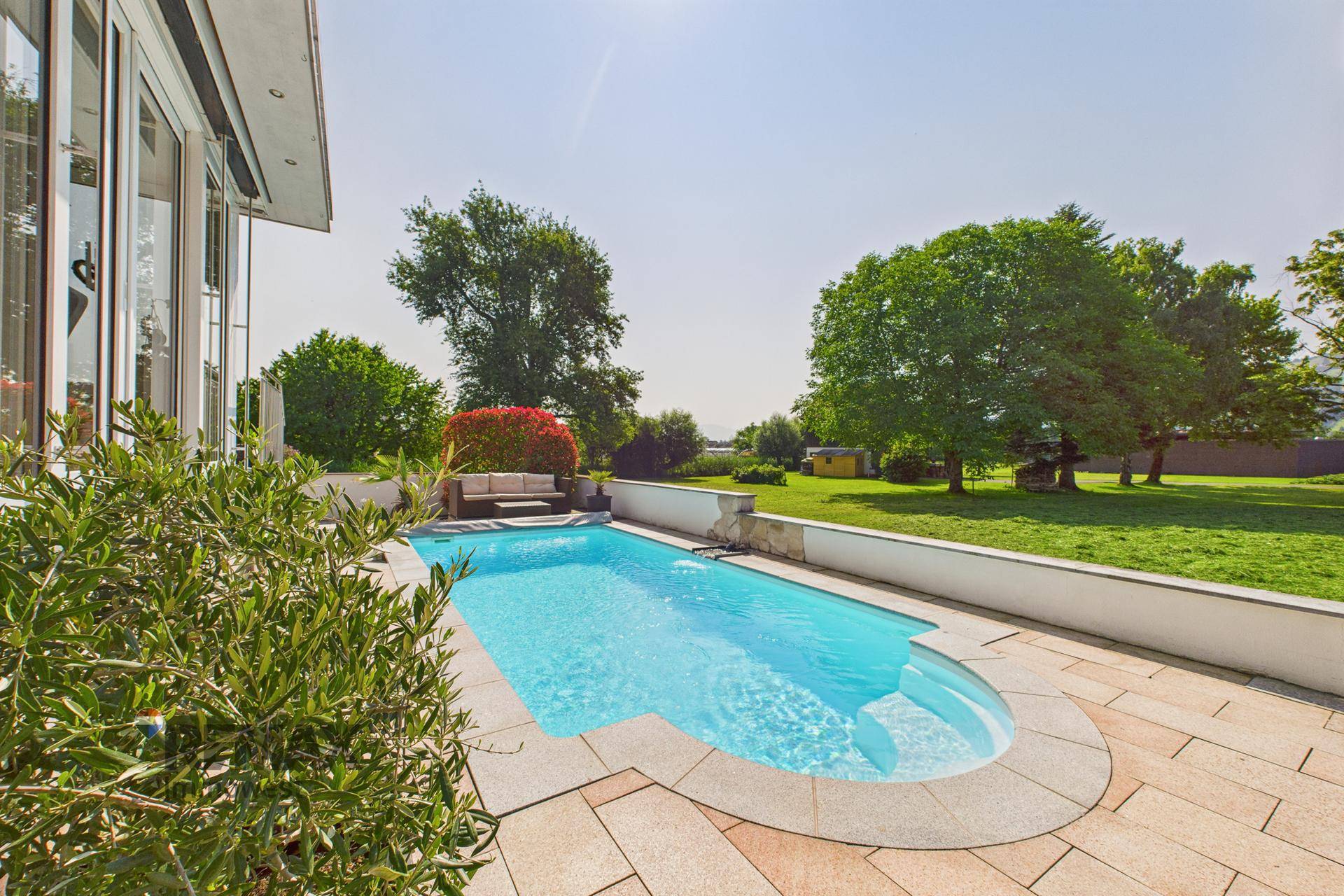 Blauer Swimmingpool mit gefliester Terrasse und weitem Blick ins Grüne.