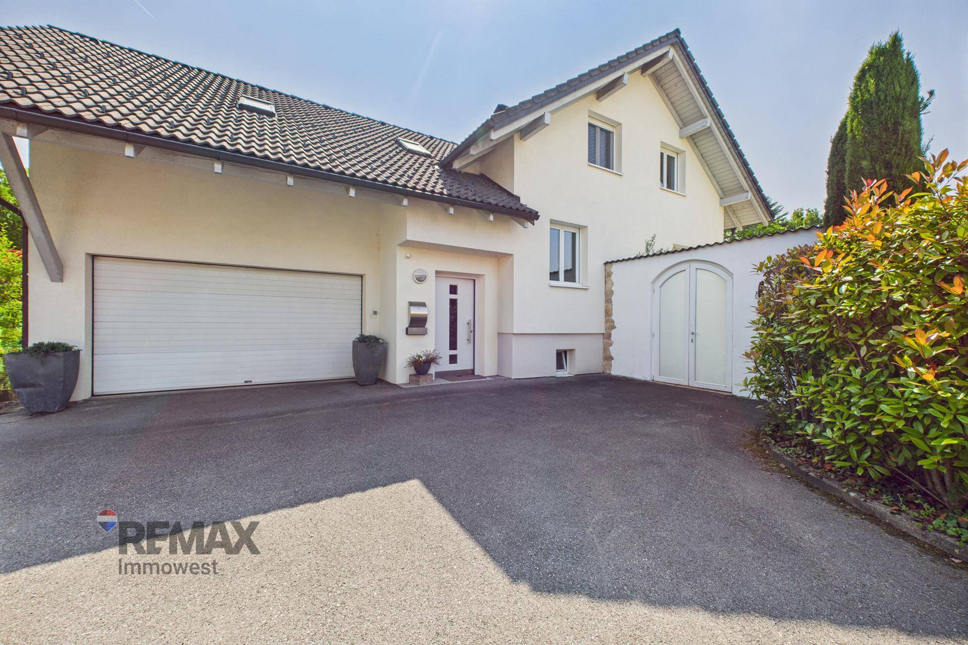 Eingangsbereich des Hauses mit großer Garage, gepflasterter Einfahrt und gepflegter Bepflanzung.