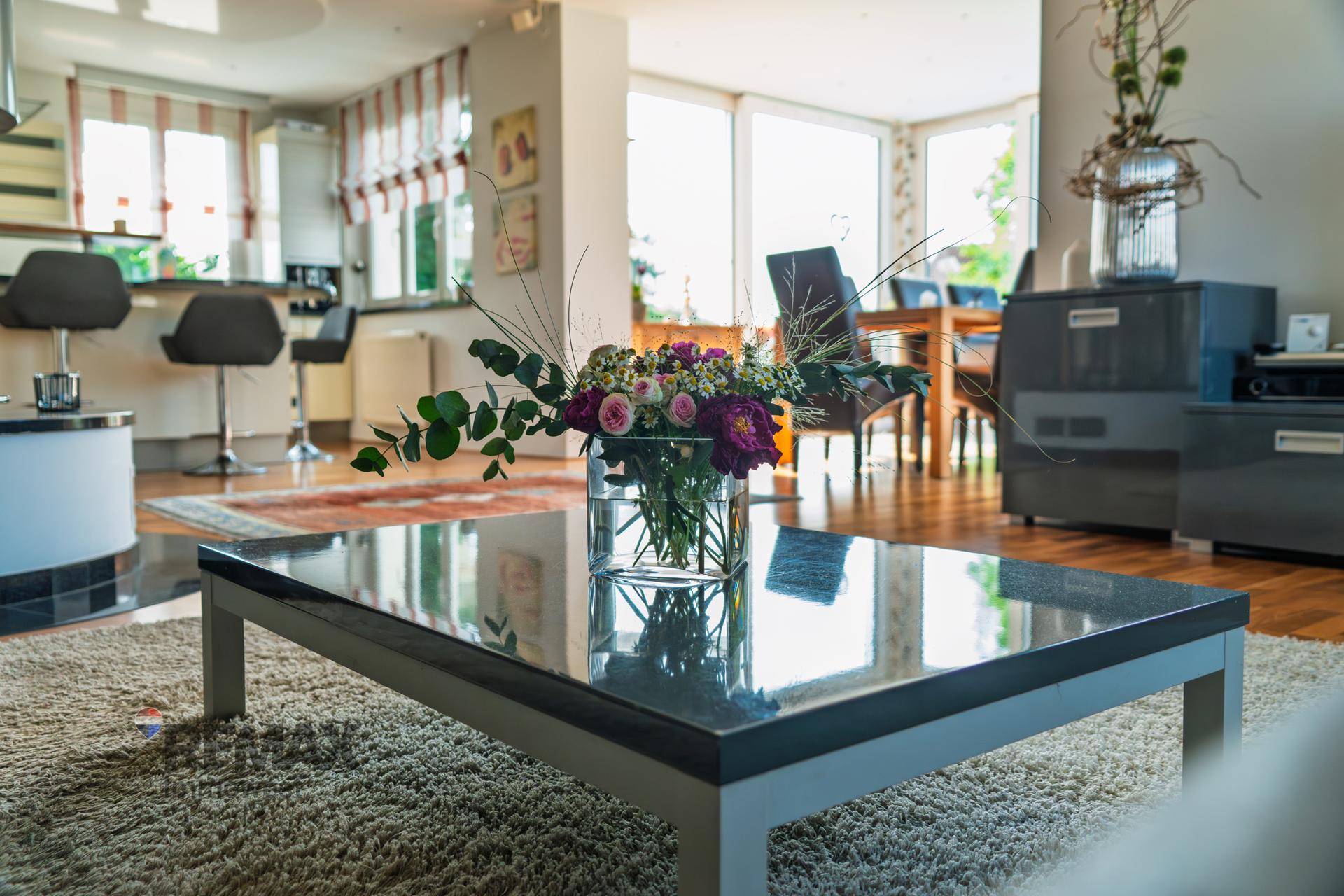 Offener Wohnbereich mit Couchtisch, Blumenarrangement und Blick auf Küche und Essbereich.