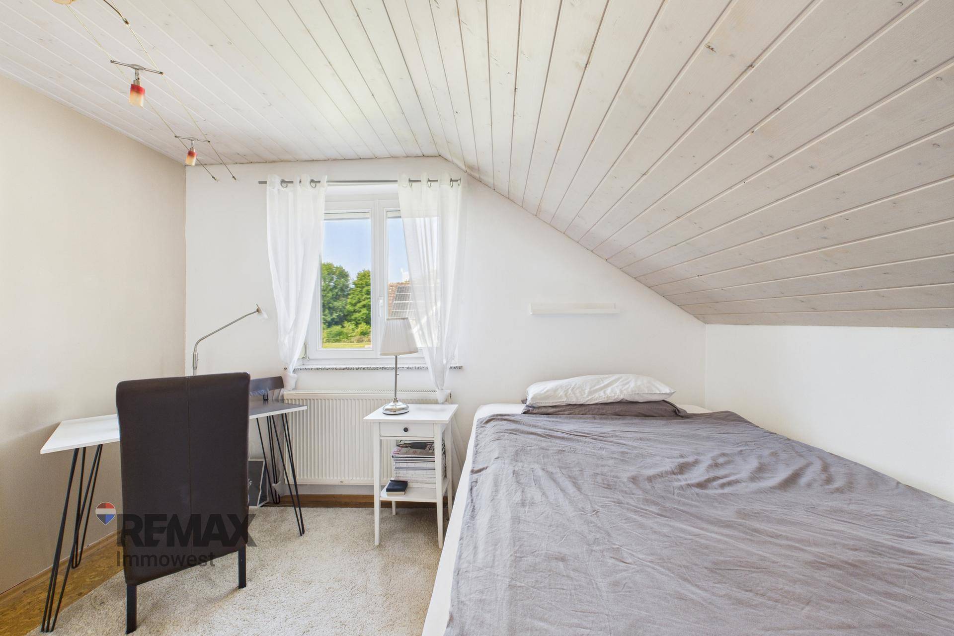 Gemütliches Schlafzimmer mit Einzelbett, Schreibtisch und Holzdachschräge.