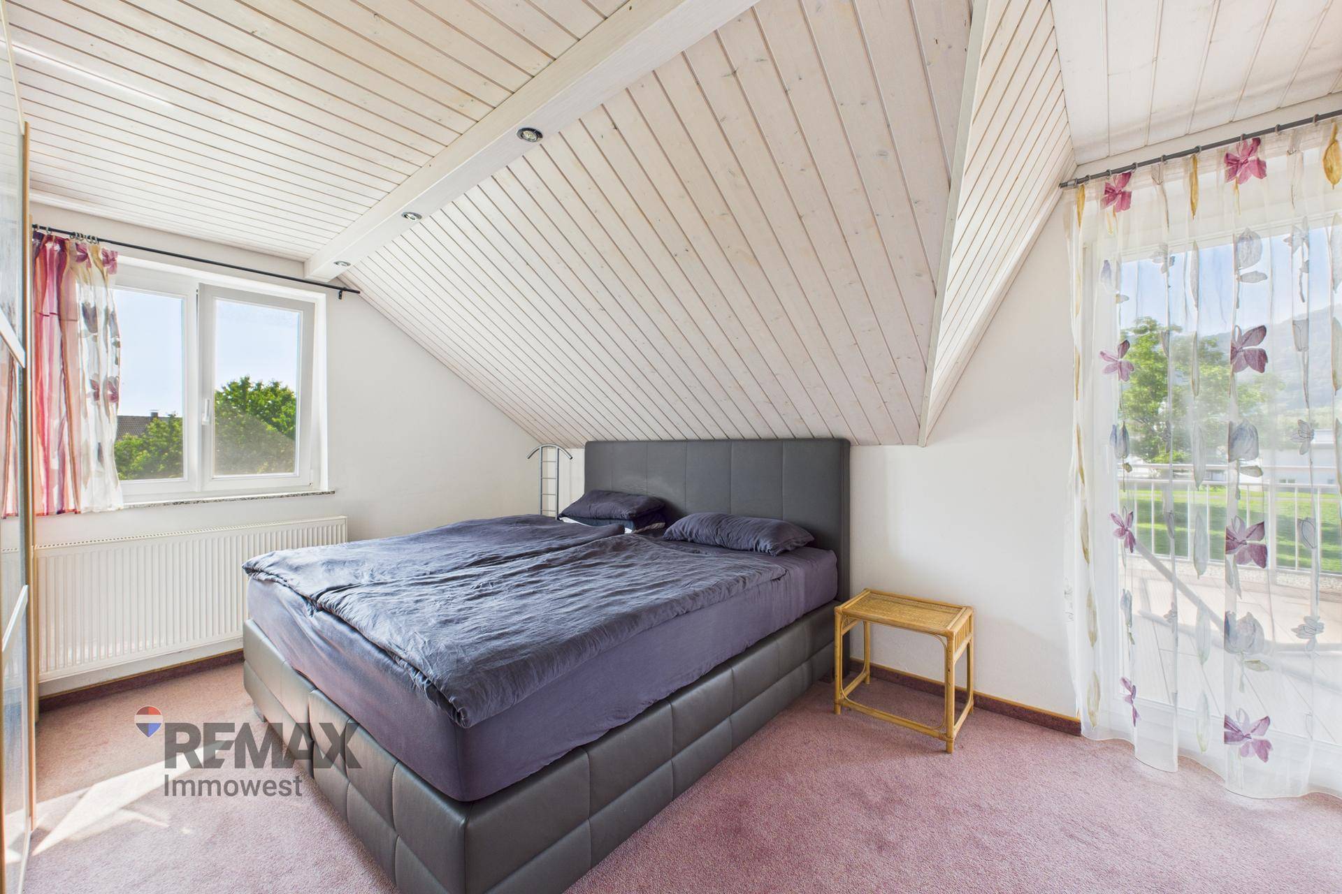 Schlafzimmer mit Doppelbett, Holzdachschräge und Fenster mit Blick nach draußen.