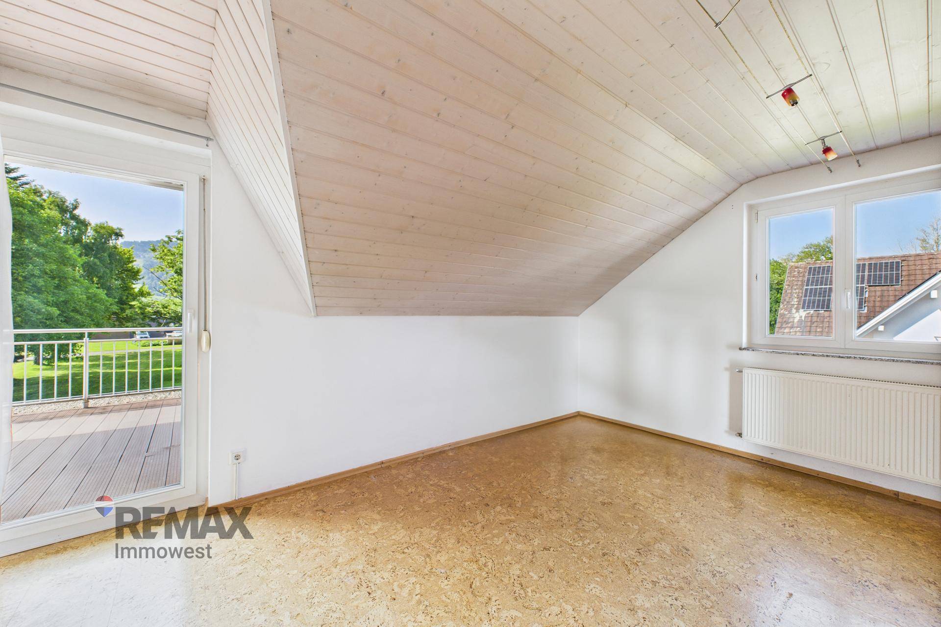 Heller Raum mit Holzdachschräge, Korkboden und Zugang zu einem Balkon.