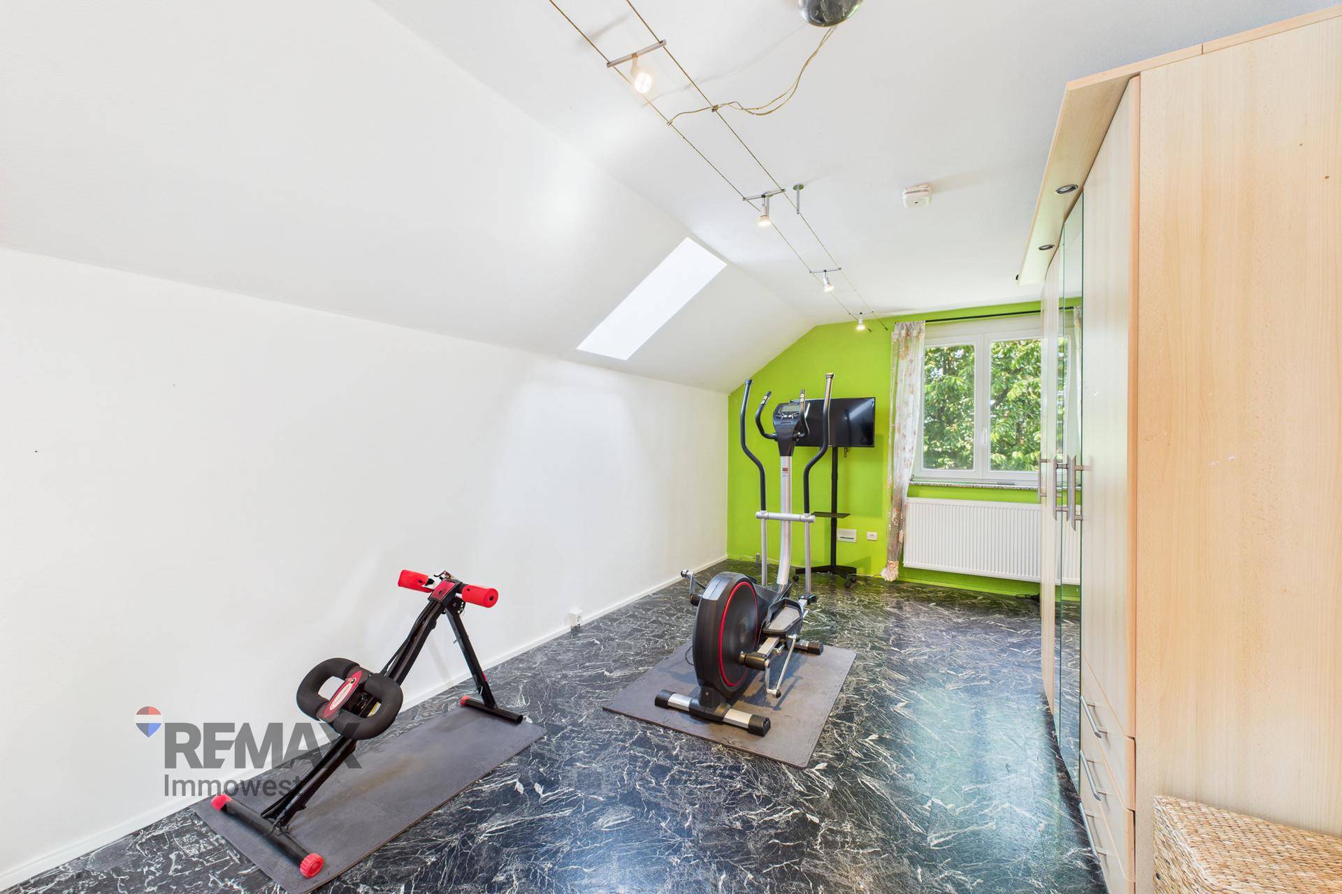 Fitnessraum mit Trainingsgeräten, Dachschräge und Fenster für natürliches Licht.