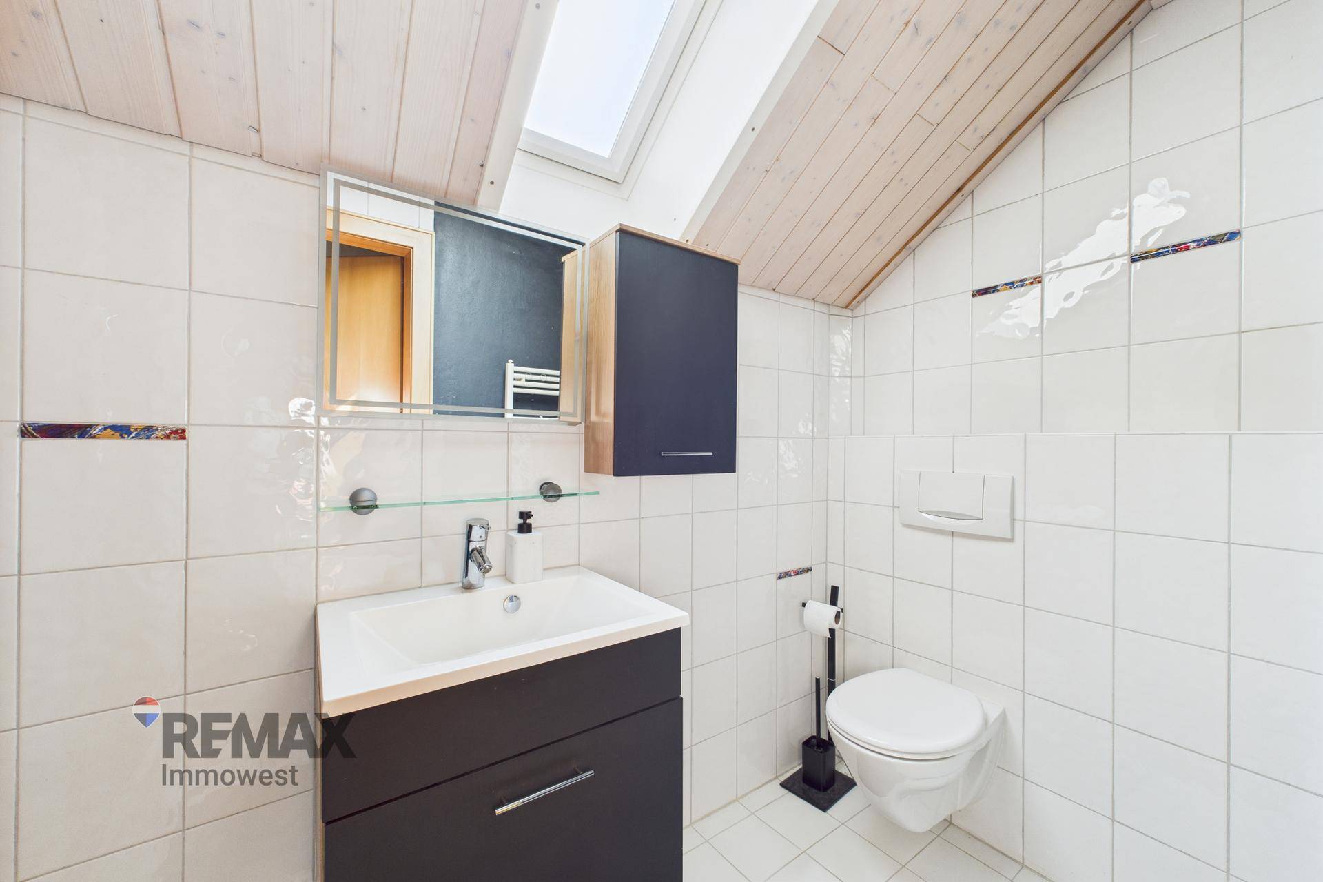 Modernes Badezimmer im Dachgeschoss mit Waschtisch, WC, weißen Fliesen und Dachfenster.