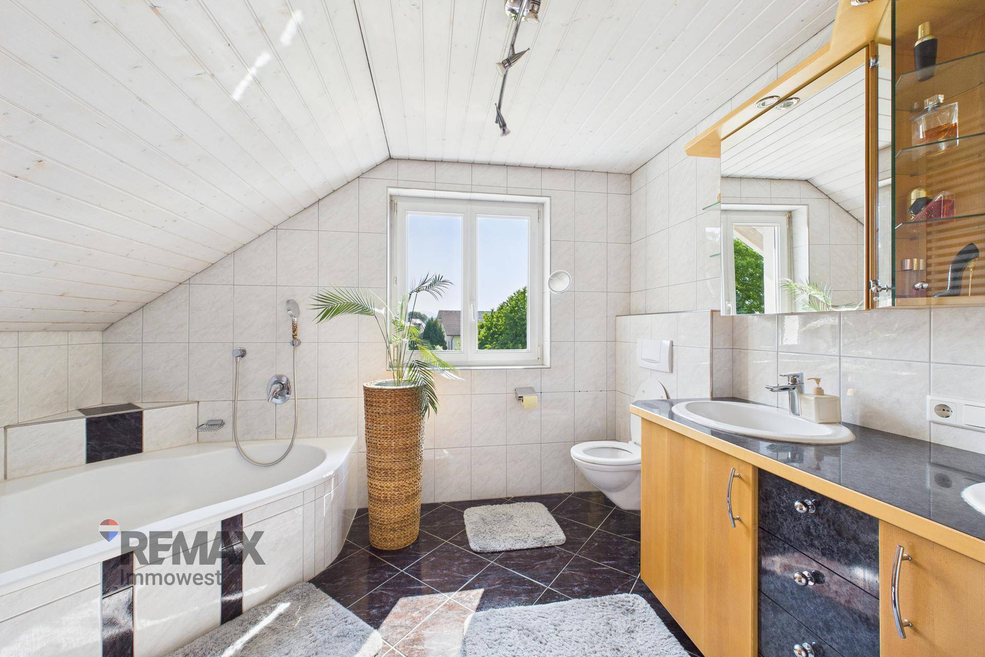 Geräumiges Badezimmer mit Eckbadewanne, Waschtisch, WC und Fenster mit Blick ins Grüne.
