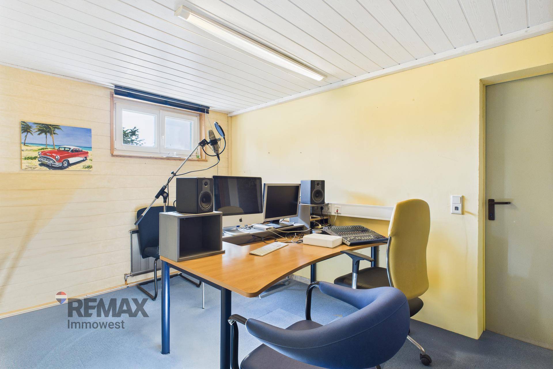 Funktionaler Büroraum mit Computern, Schreibtisch, gelben Wänden und Fenster.