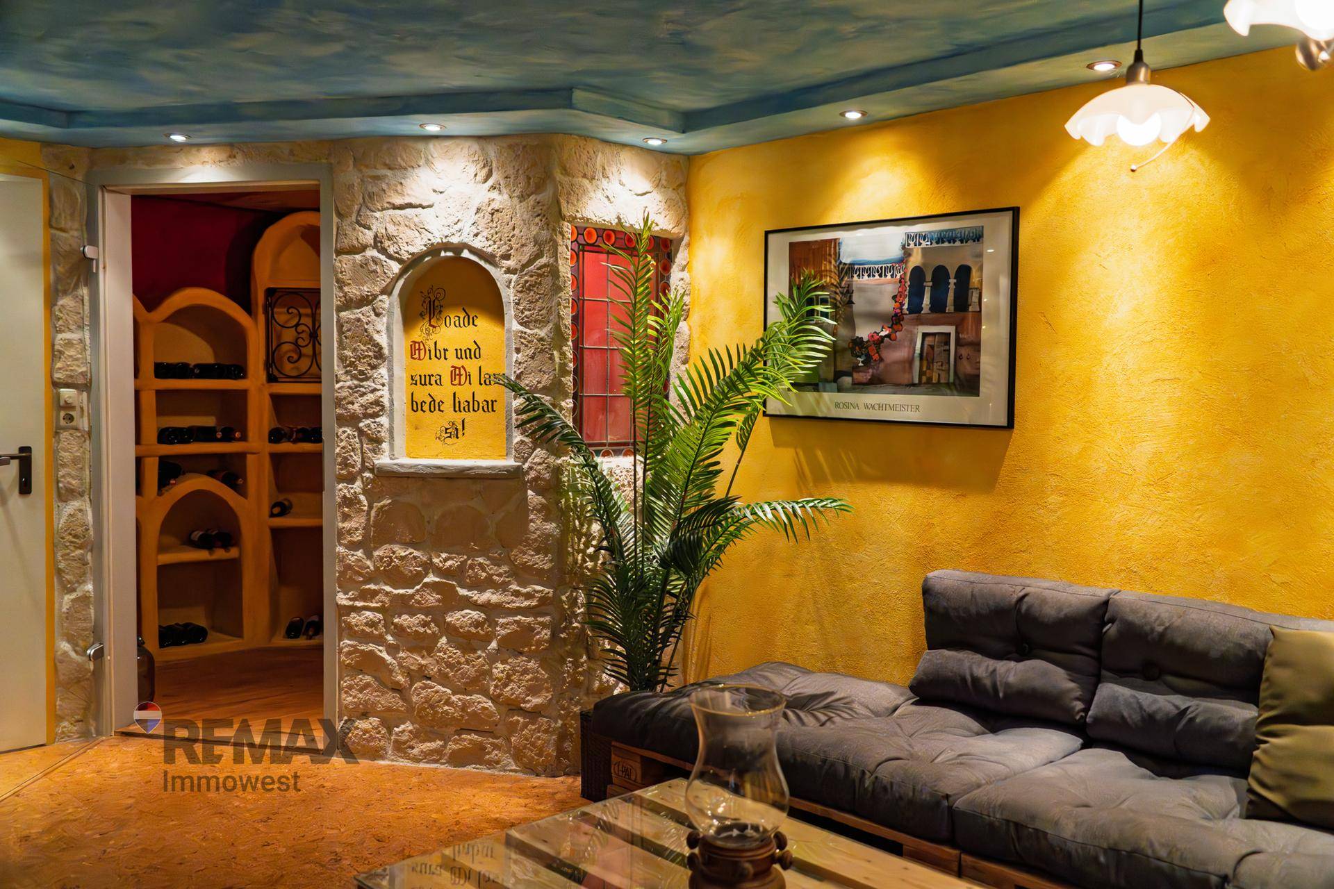 Gemütlicher Wohnbereich mit Palettensofa, Steinwand, gelben Wänden und Zugang zum Weinkeller.