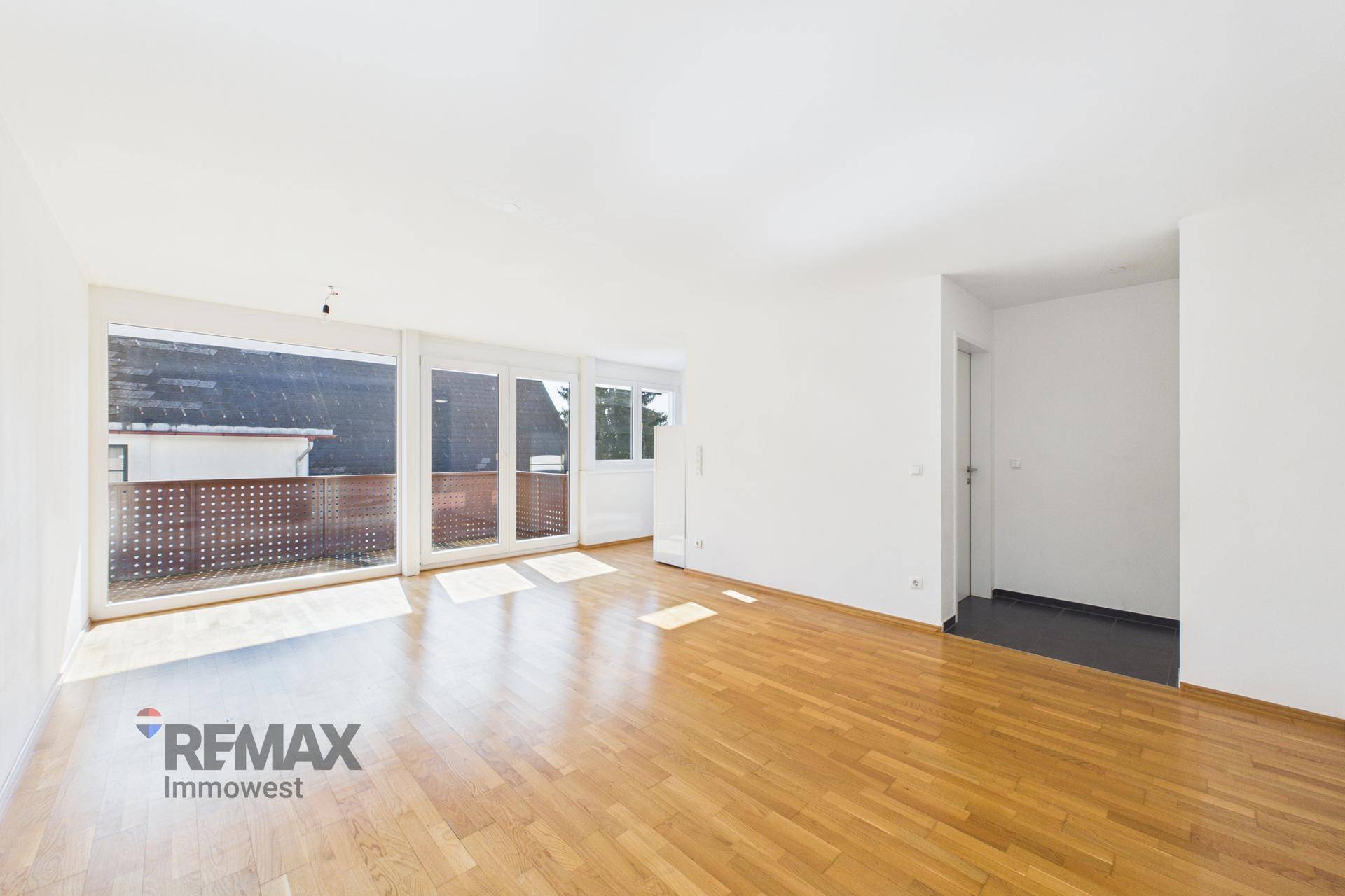 Geräumiges Wohnzimmer mit hellem Parkettboden und großen Fenstern für viel Tageslicht.