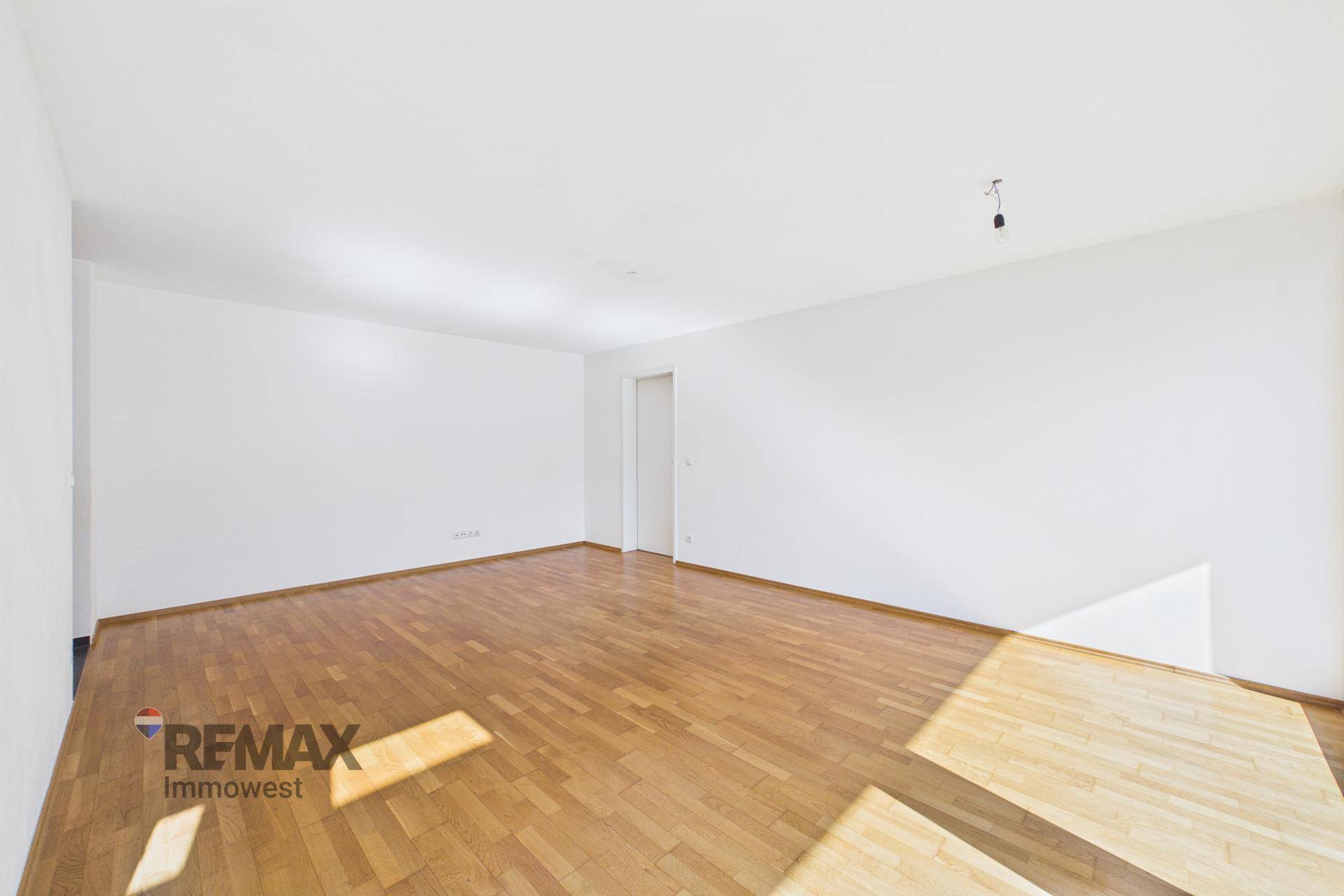 Geräumiger, leerer Raum mit hellem Parkettboden und viel Tageslicht.