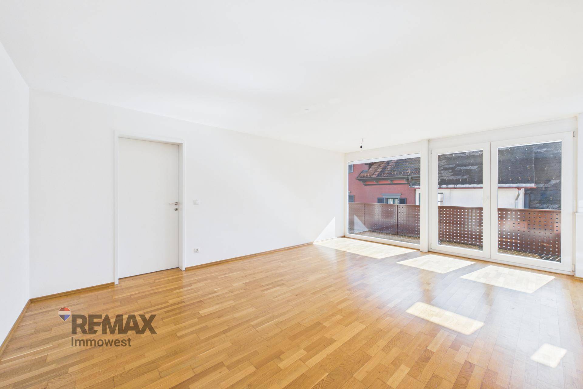 Lichtdurchflutetes Wohnzimmer mit Parkettboden und Zugang zu einem Balkon.