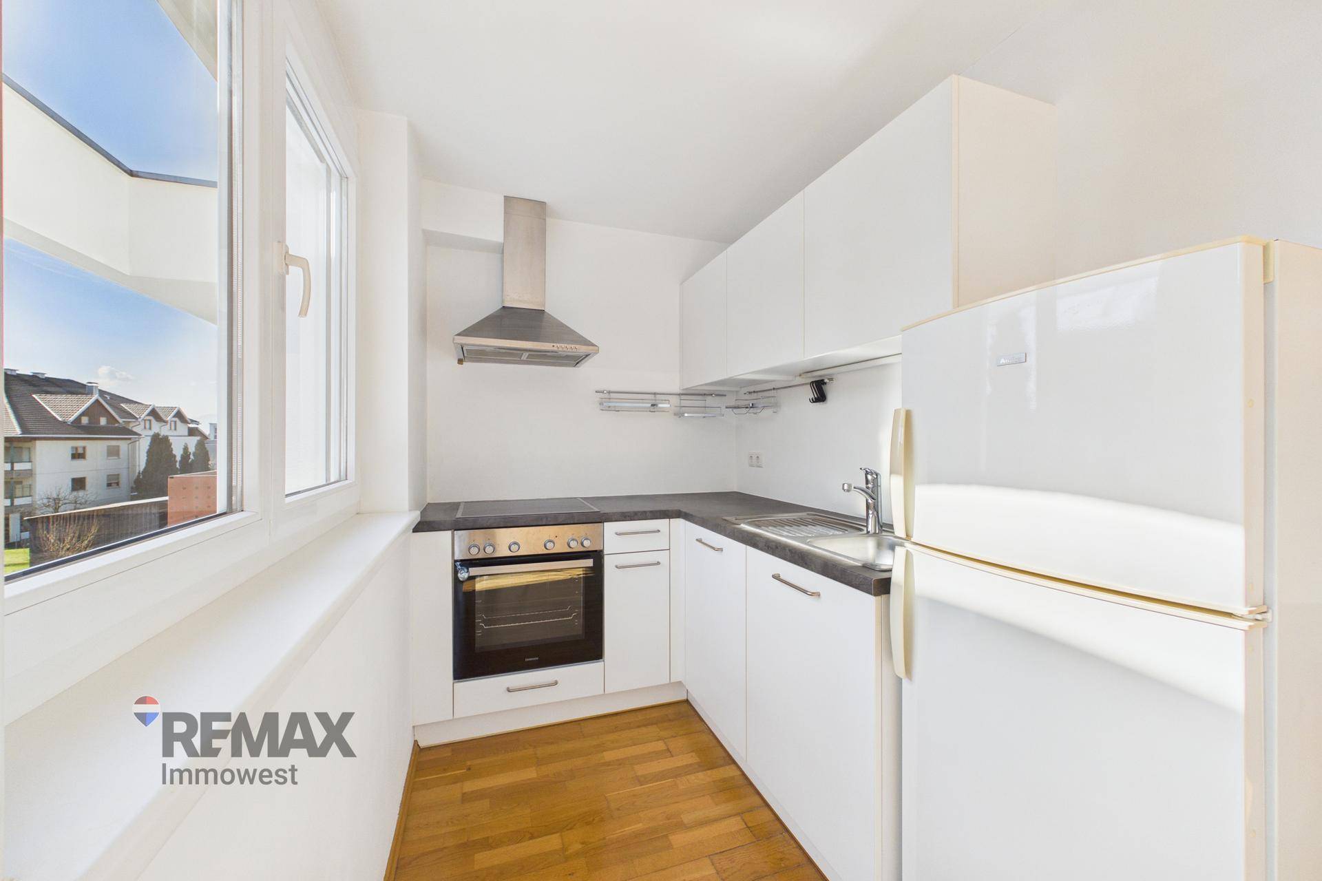 Funktionale Küche mit weißen Schränken, Backofen und Kühlschrank, hell durch Fenster.