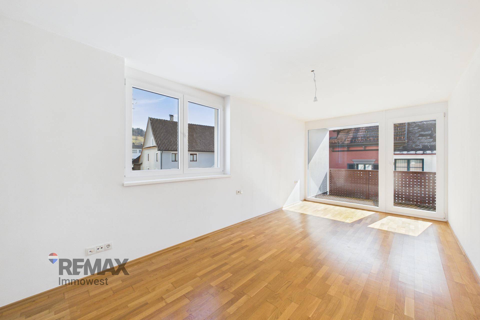 Helles Zimmer mit Parkettboden und Fenster, bietet Zugang zu einem Balkon.