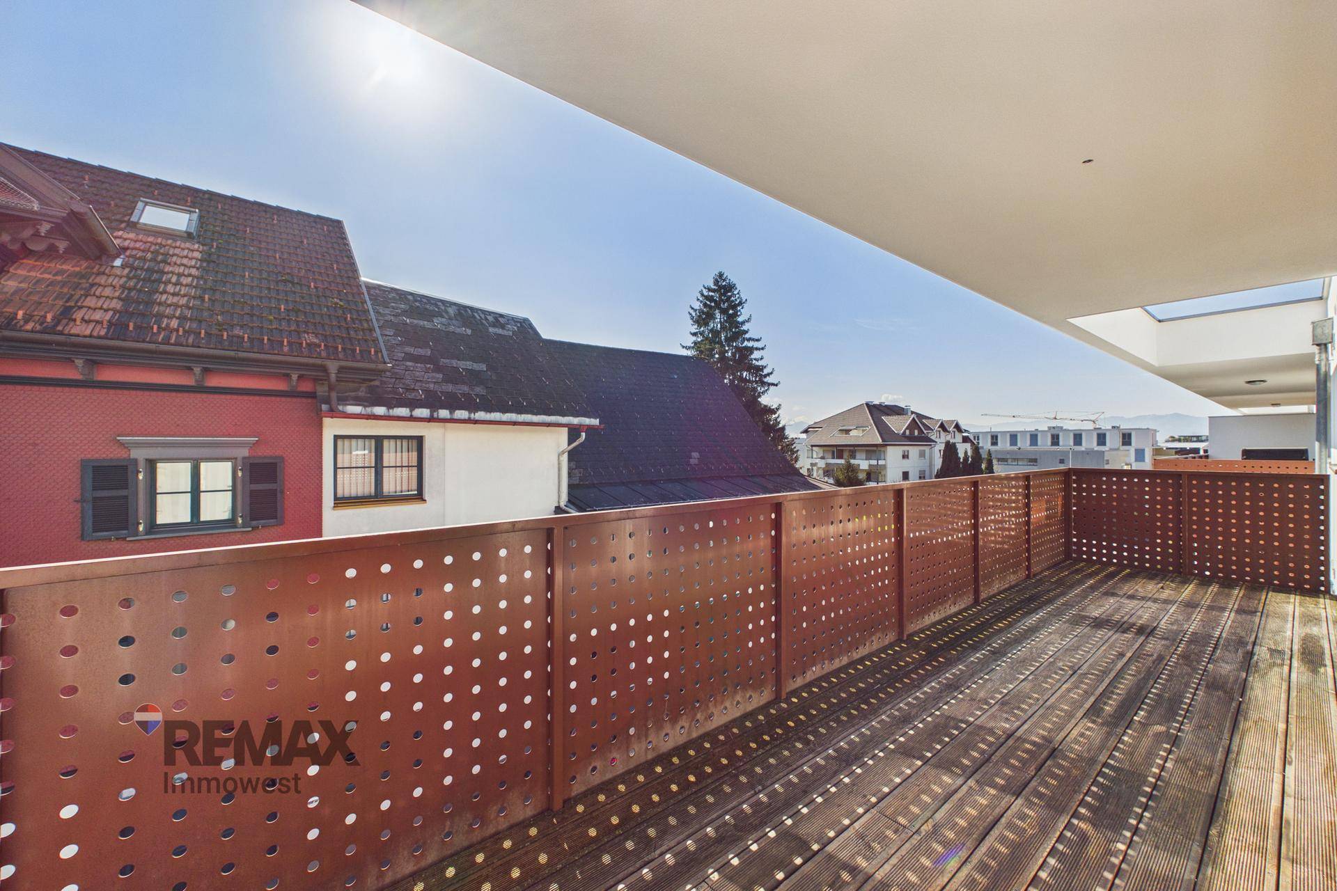 Großer Balkon mit Holzboden und moderner Lochblech-Brüstung, sonnig und hell.
