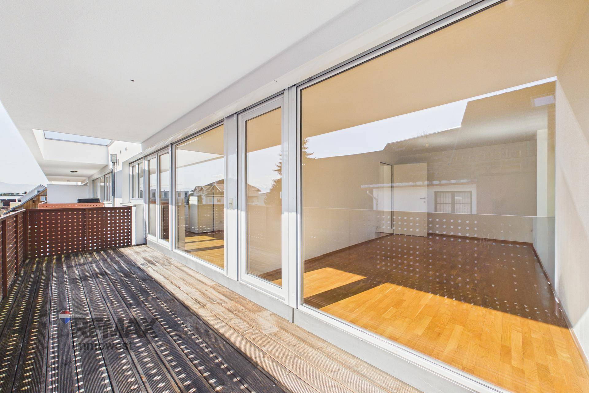 Geräumiger Balkon mit Holzboden und großen Fenstern zum Innenraum.