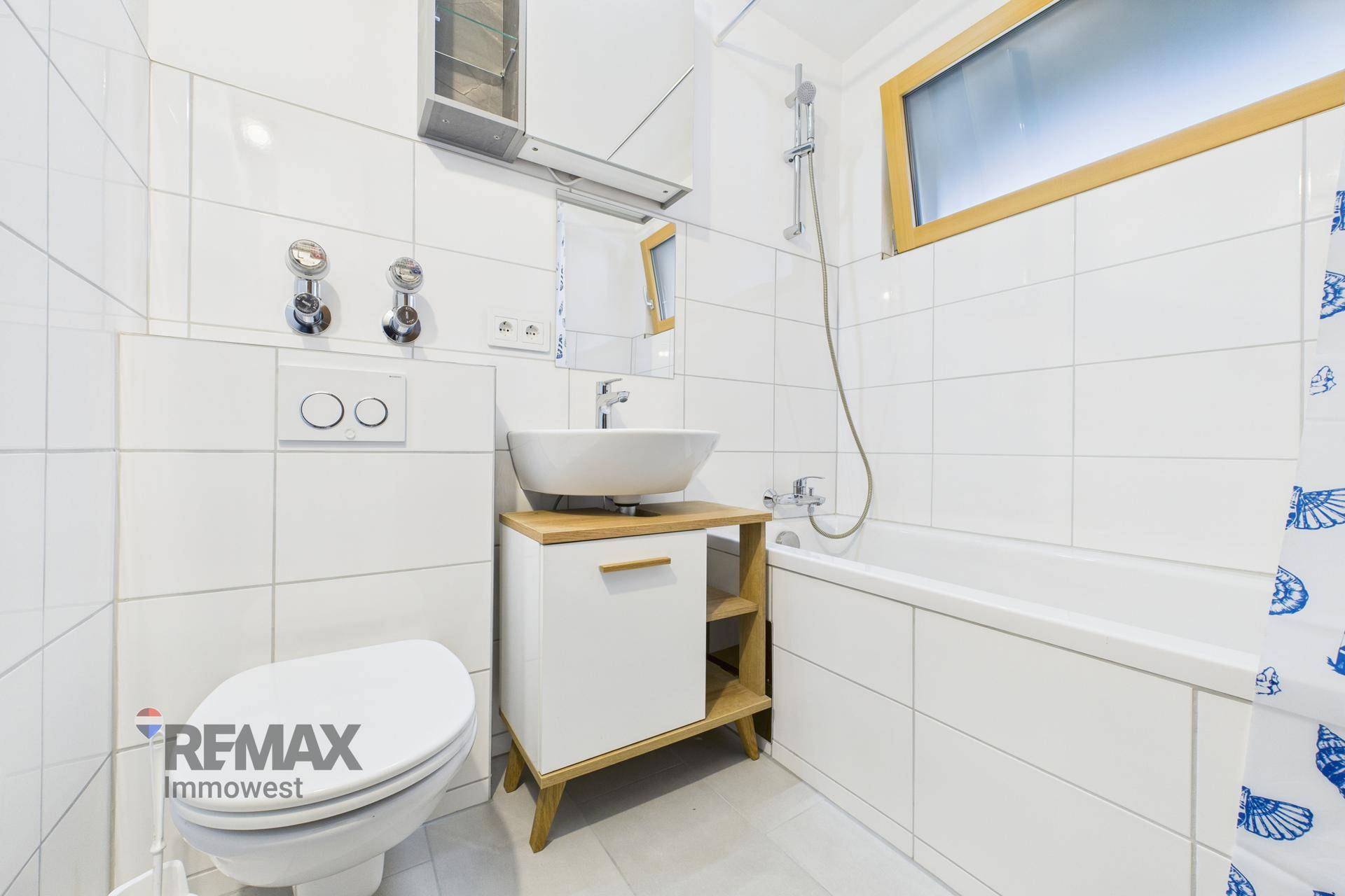 Modernes Badezimmer mit weiß gefliesten Wänden, wandhängender Toilette, Waschbecken und Badewanne.