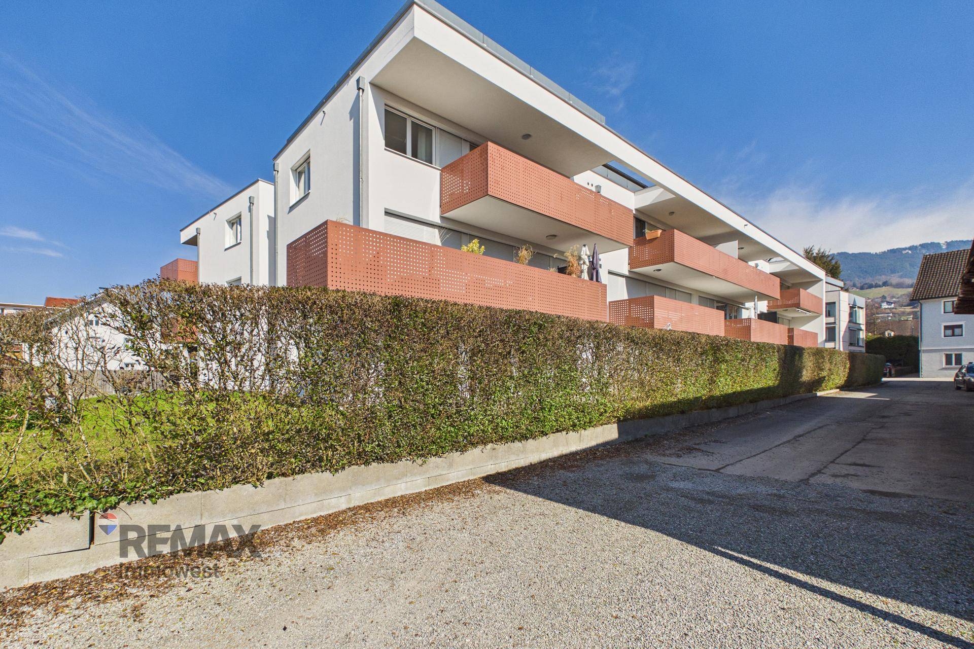 Modernes Mehrfamilienhaus mit Balkonen und gepflegter Außenanlage unter blauem Himmel.