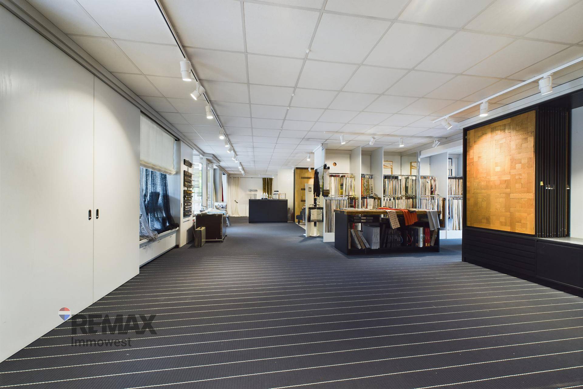 Weitläufiger Ausstellungsraum mit gestreiftem Teppichboden und zahlreichen Präsentationsflächen für Materialien und Stoffe.