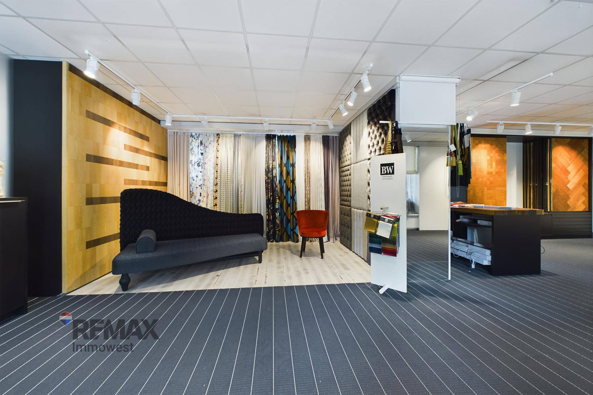 Heller Ausstellungsraum mit einer eleganten Chaiselongue, Holzwänden und einer Vielzahl von Stoff- und Materialproben.