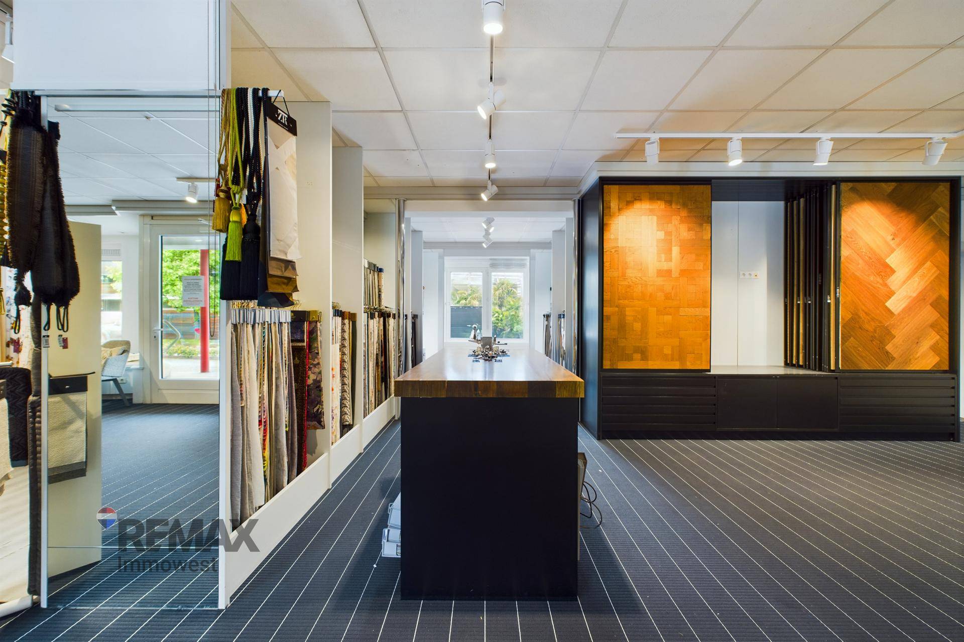 Moderner Ausstellungsraum mit einem Holztresen und Mustern für Bodenbeläge und Textilien, Blick zum Ausgang.