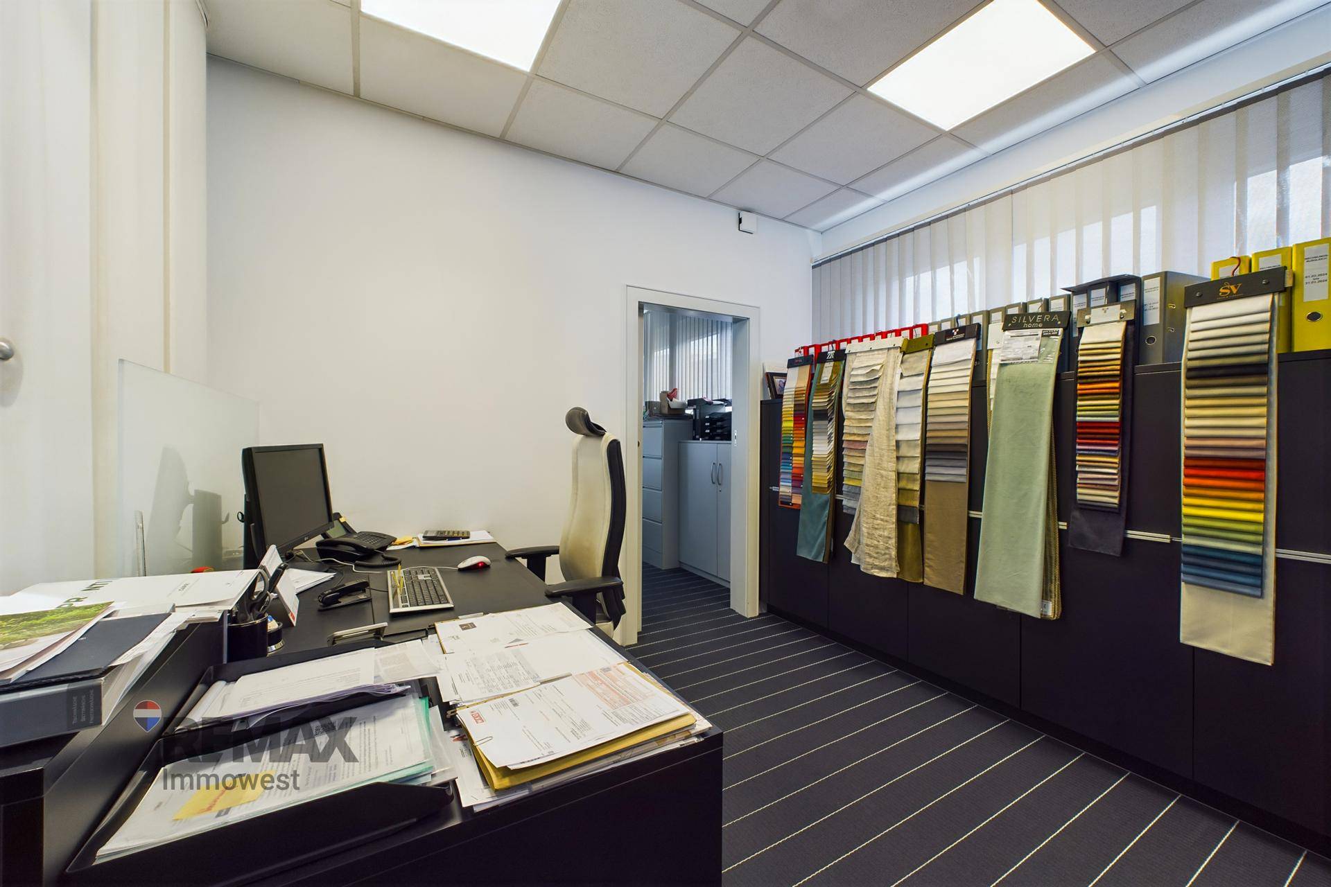 Funktionales Büro mit einem Schreibtisch, Computer und Regalen voller Stoffmuster für die Kundenberatung.